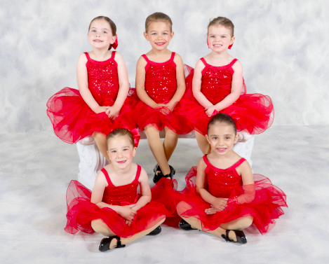 Five young girls dressed in red ballet costumes, sitting and standing against a white background.