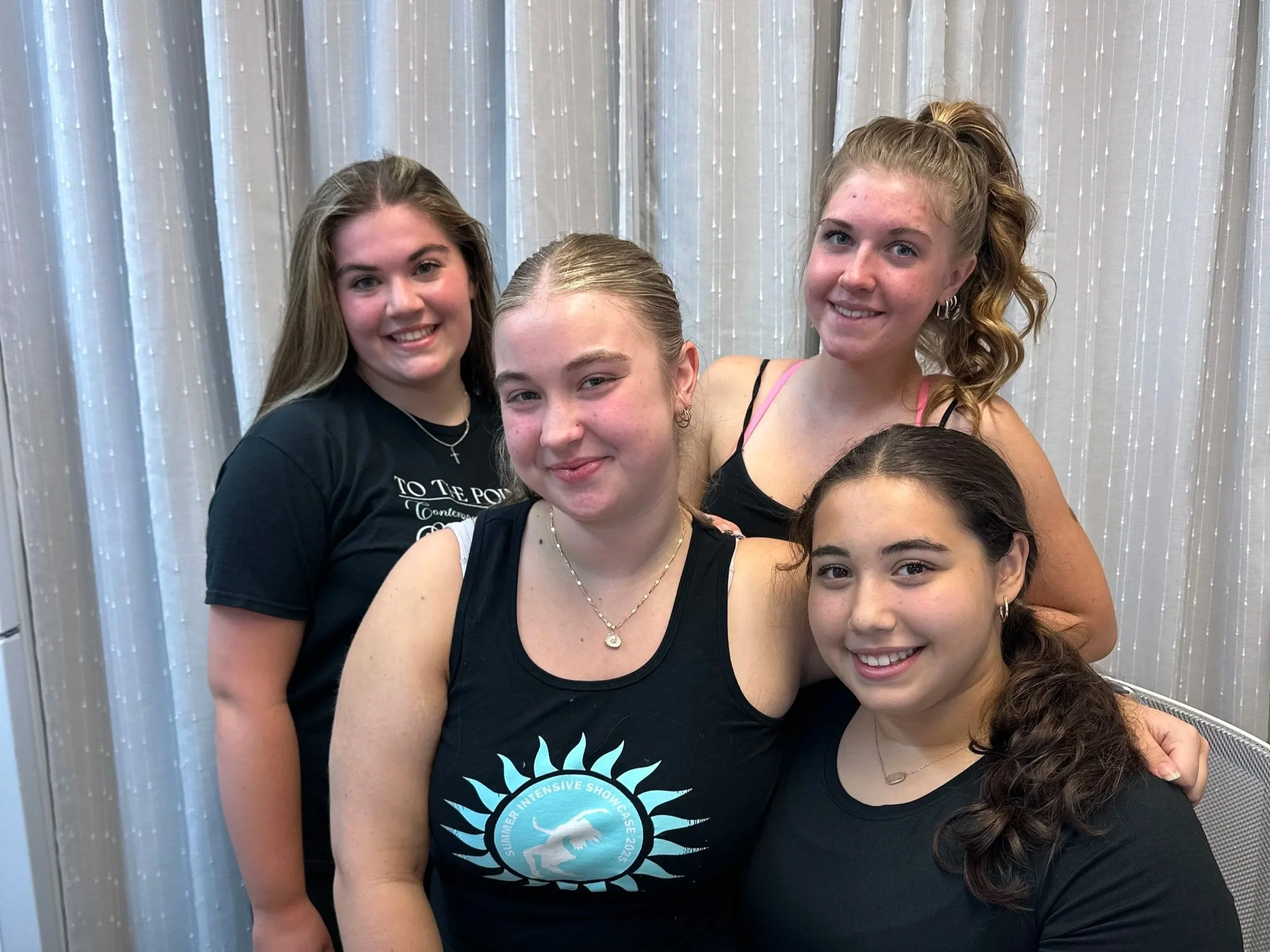 Five teenage girls posing together indoors in front of a light-colored curtain, smiling at the camera.
