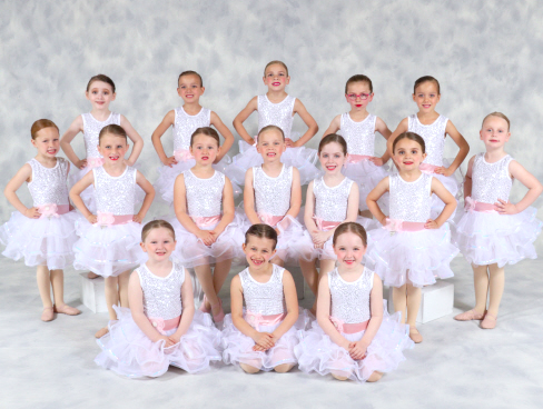 Group of young girls dressed in white ballet costumes posing for a photo in a dance studio.