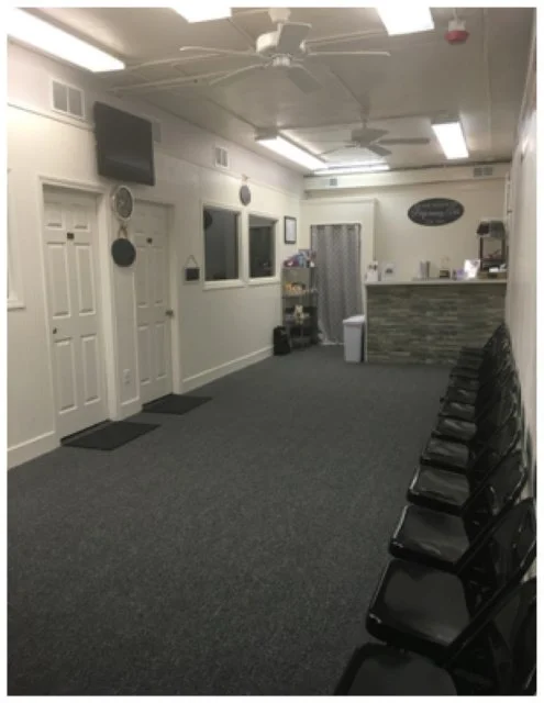 Empty waiting room with black chairs arranged along the right wall, a service counter at the back, and a gray carpeted floor.