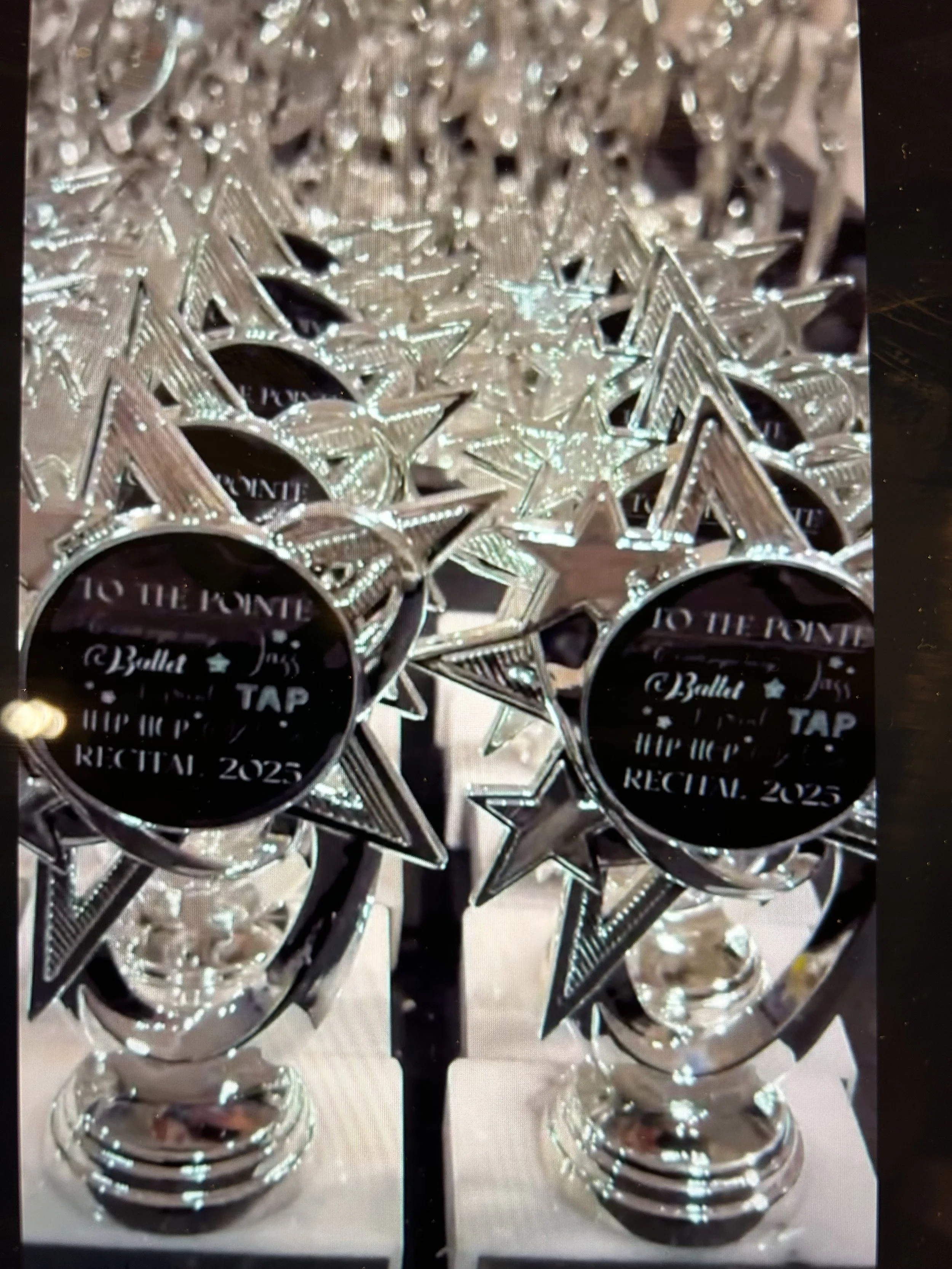 Collection of speaker trophies with star and circle shapes, featuring black labels with white text that read, "To the Point," "Ballet Tap," "Hip Hop," in large print, and the year "2025."
