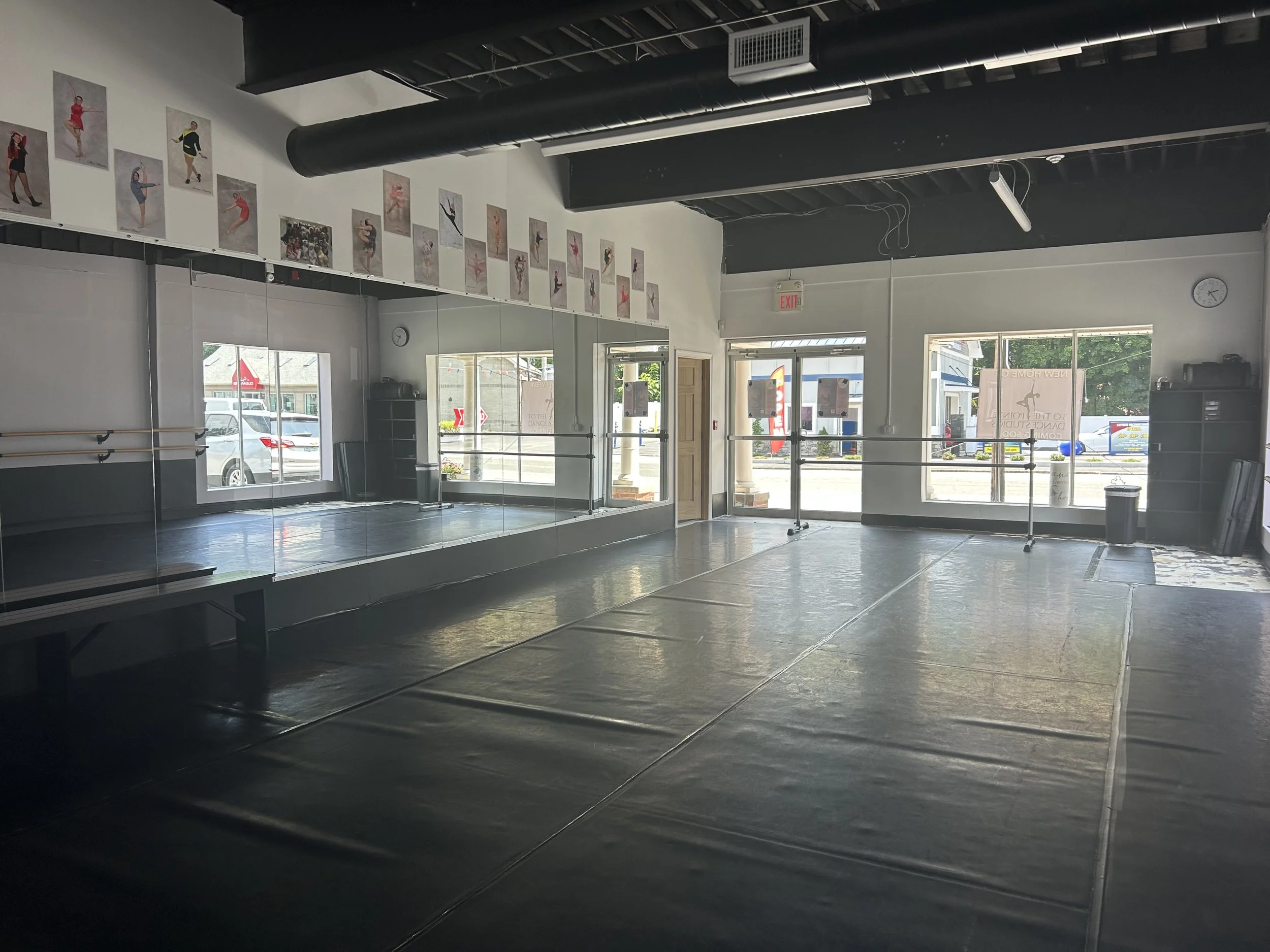 An empty dance studio with mirrors, ballet barres, and posters of dancers on the wall, sunlight coming through the windows.