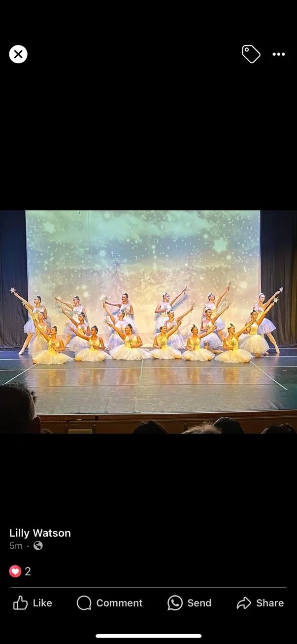 A group of ballerinas performing on stage, dressed in white tutus and golden tops, with a colorful and sparkling background projection.