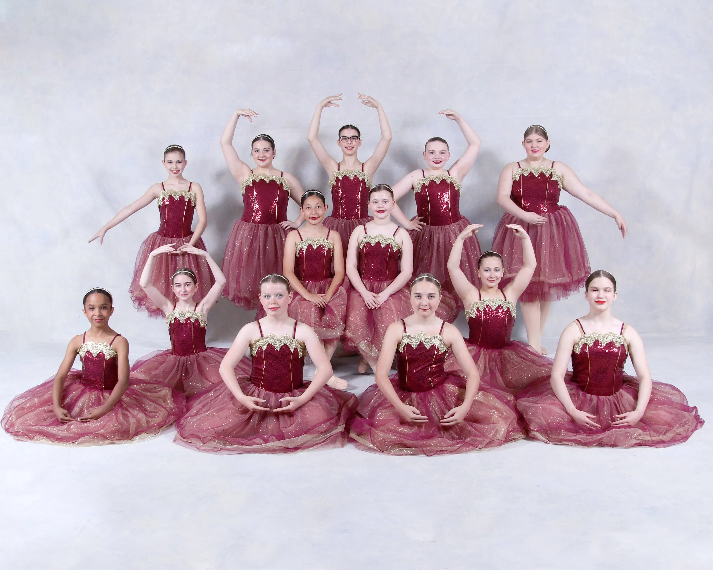Six young female dancers in pink costumes with floral accents performing a coordinated ballet pose against a neutral backdrop.