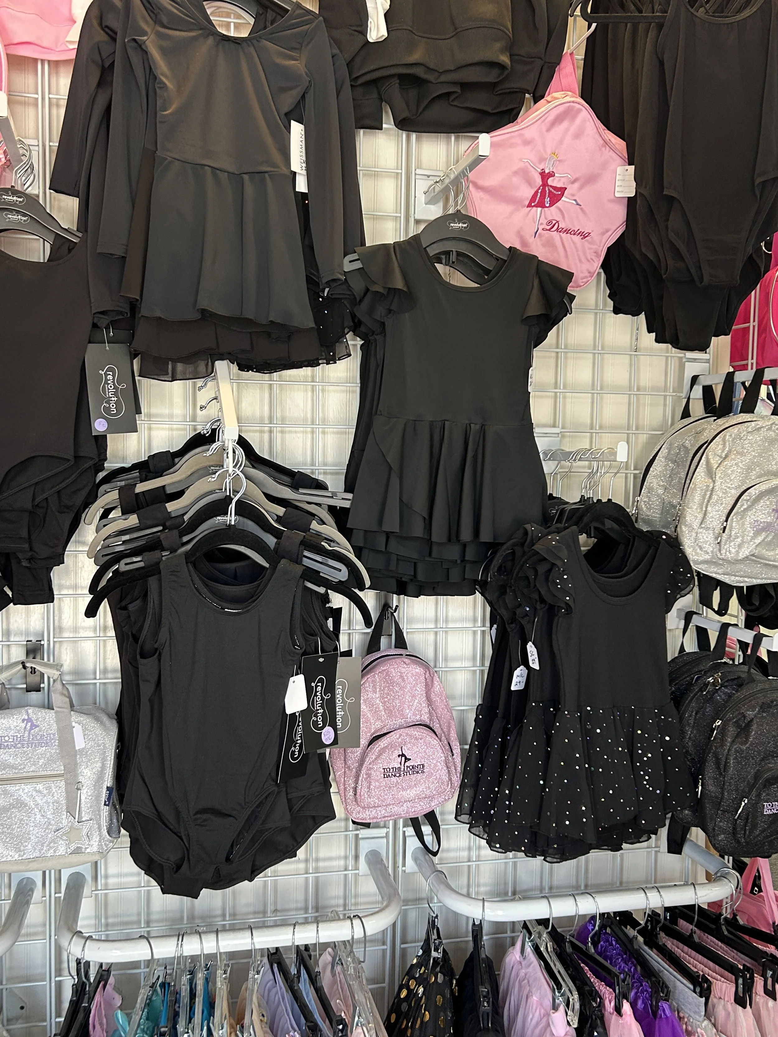 Display of black dance costumes, leotards, skirts, and backpacks at a retail store.