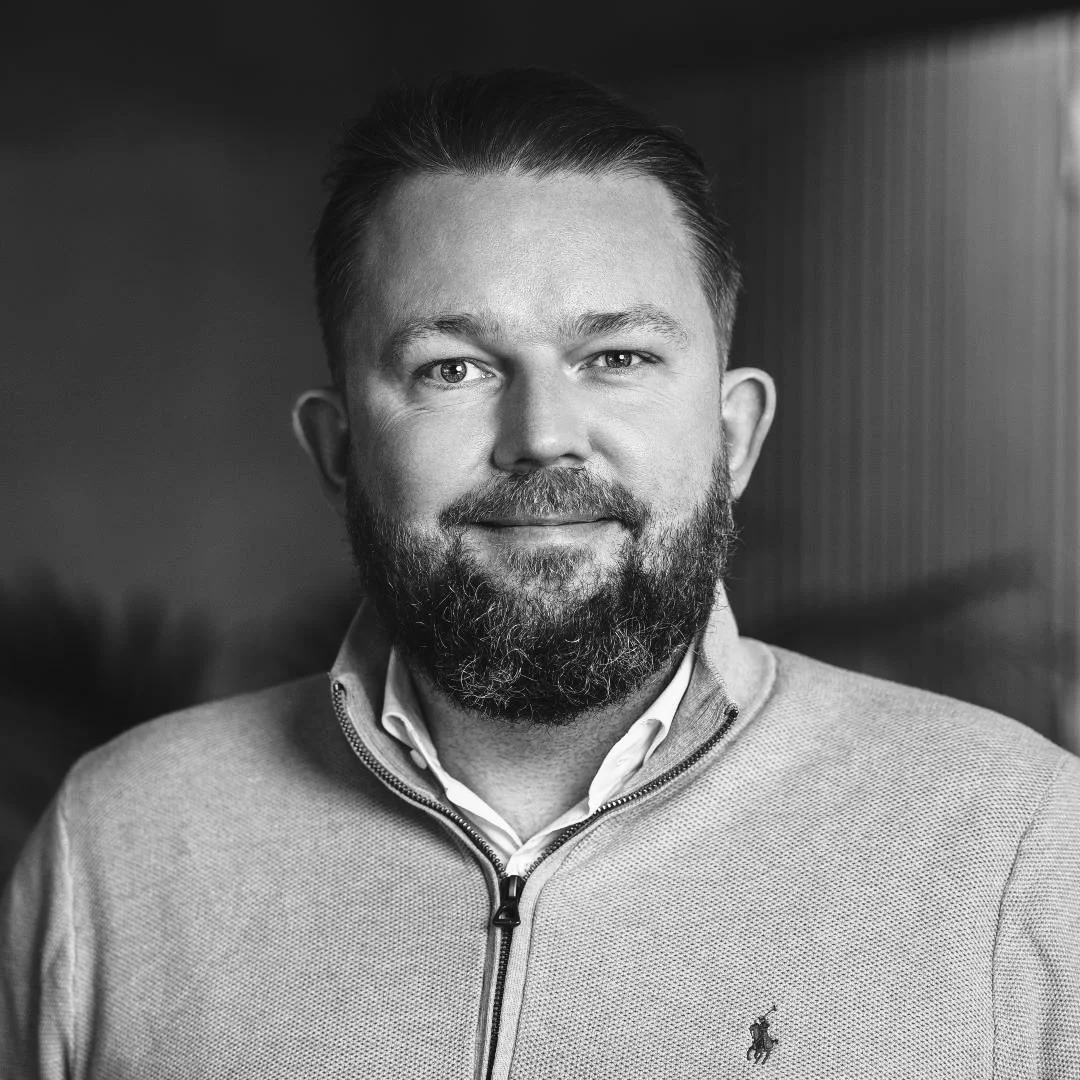 Black and white portrait of a smiling man with a beard, wearing a quarter-zip sweater and collared shirt.