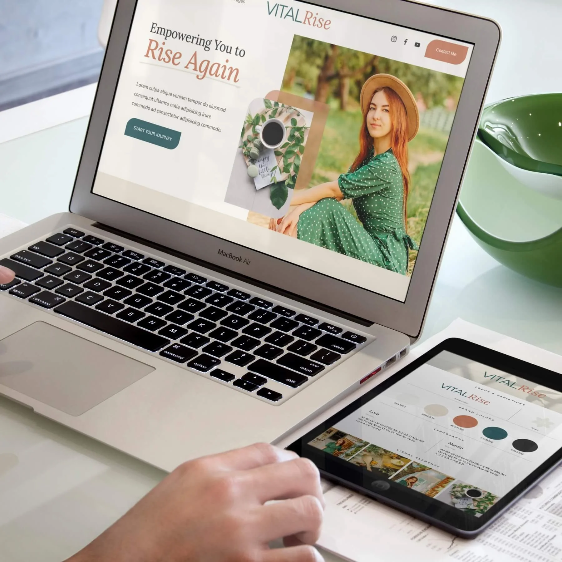 A person holding a smartphone displaying a website titled 'VITAL Rise' with a photo of a woman in a green dress and hat, sitting outdoors, across from a laptop showing the same website and a printed color palette sheet titled 'VITAL Rise' on a white table next to a green coffee mug.