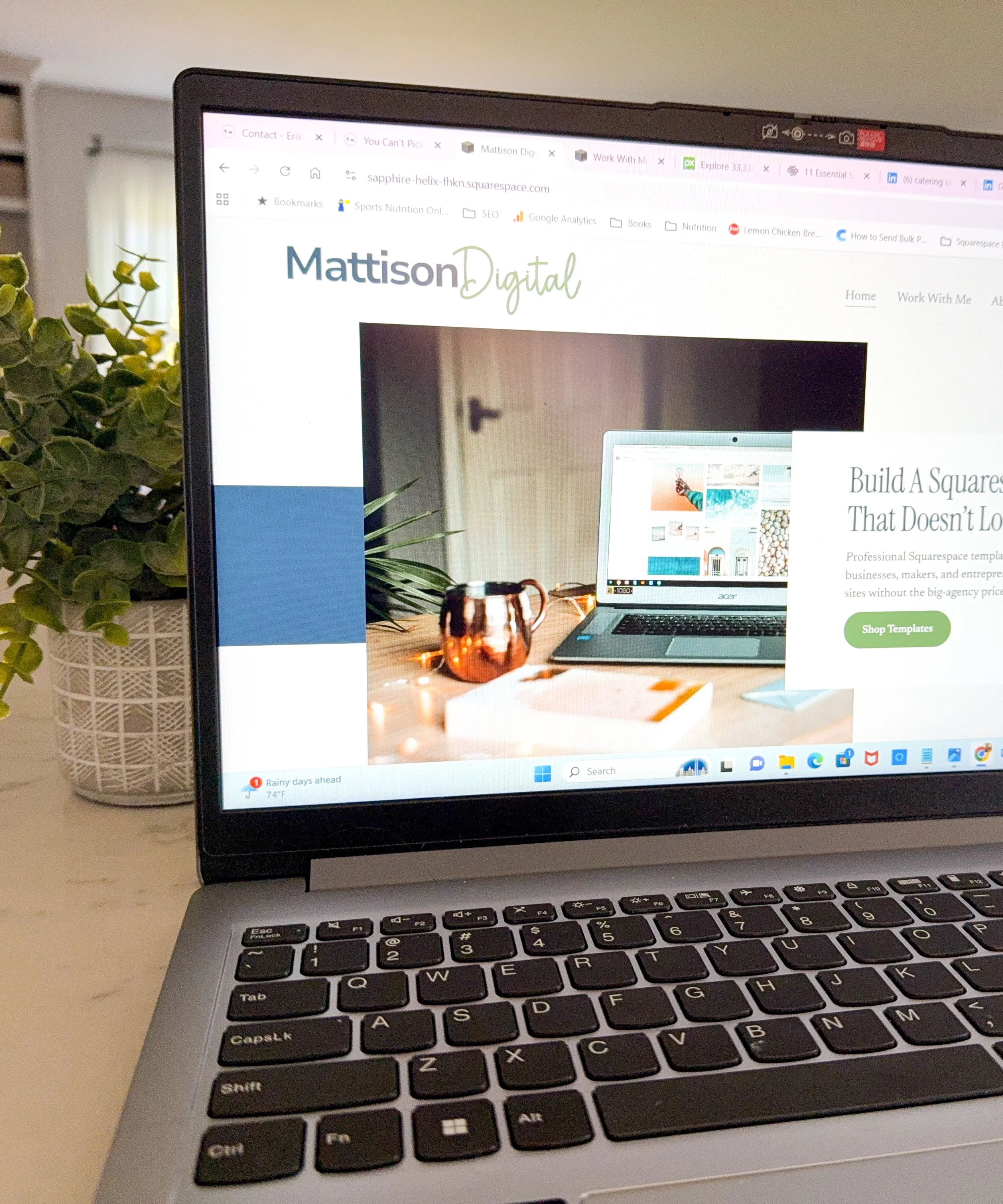 Close-up of a laptop with a black keyboard and a screen displaying a website called Mattison Digital, with a houseplant in a white woven basket on the left side of the desk.