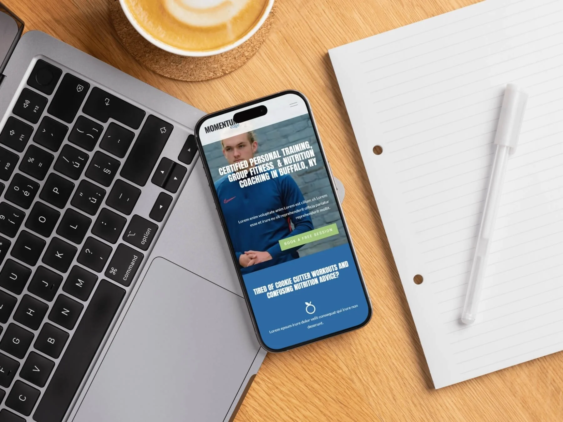 Smartphone displaying a fitness coaching website on a wooden desk with a silver laptop, a notebook with a pen, and a coffee cup.