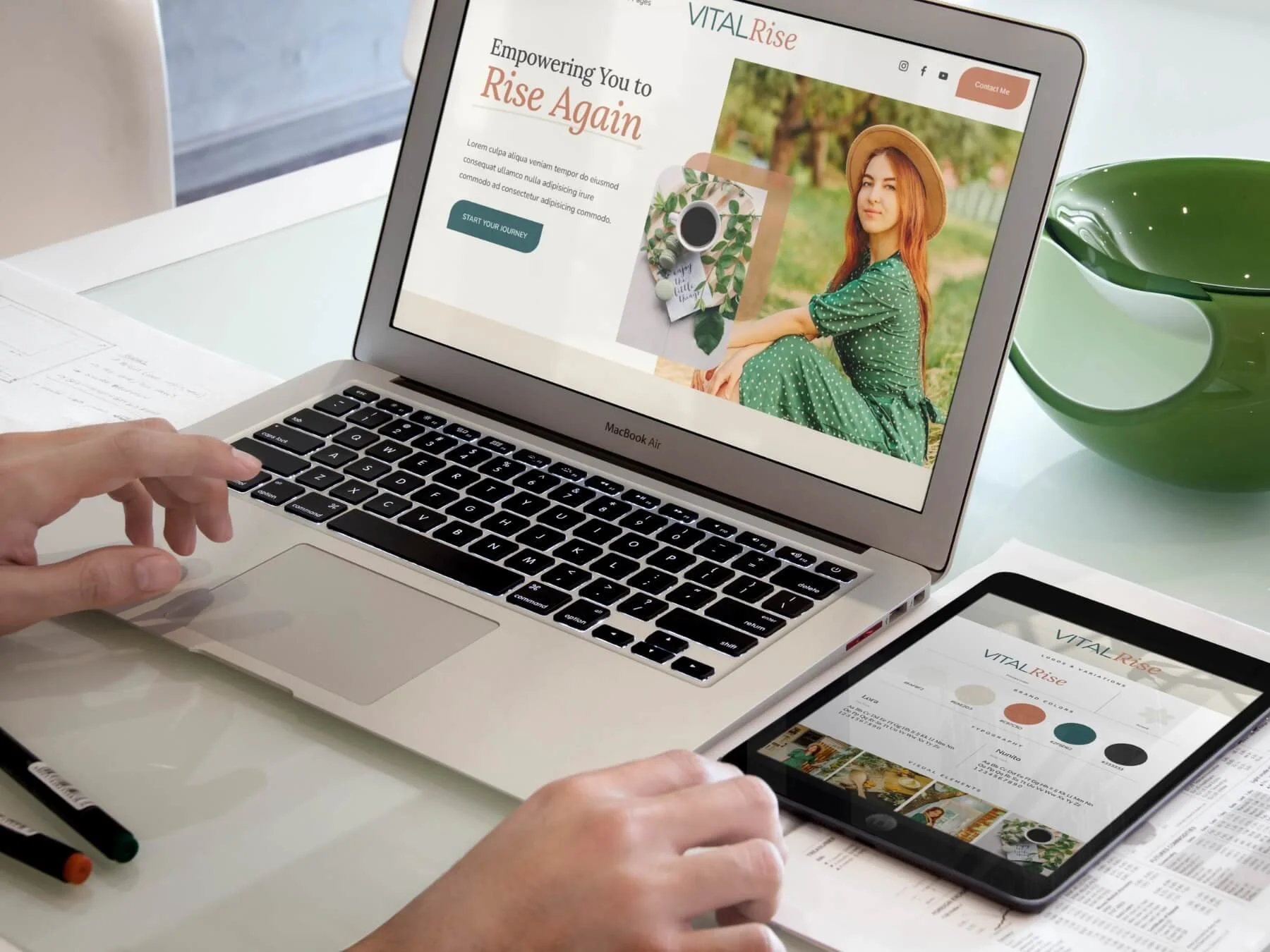 A person working on a laptop and tablet displaying the Vital Rise website, which features a woman in a green dress with red hair and a hat, outdoors in a park setting.