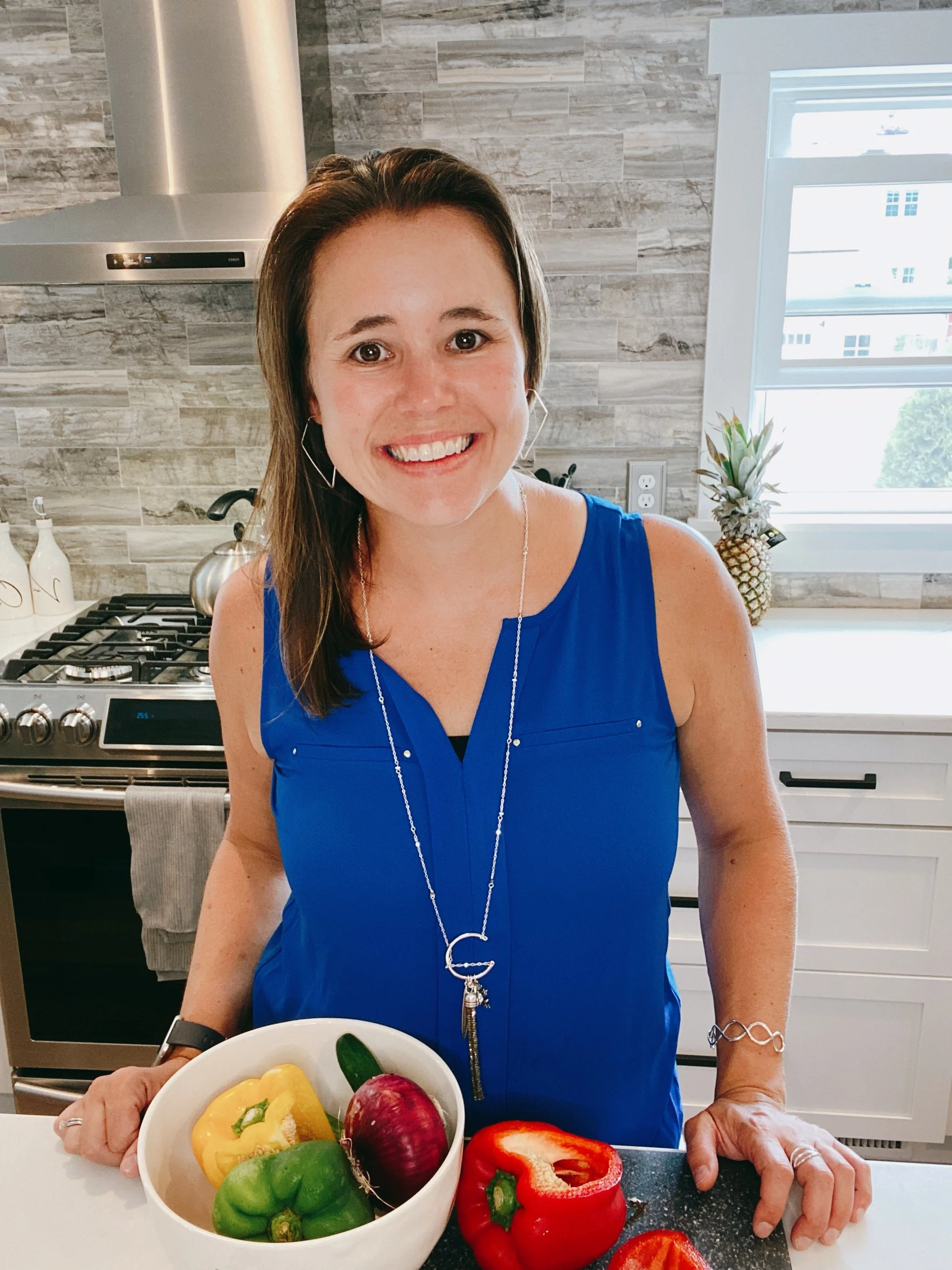 Marcie Baranich, owner of Mattison Digital, in a kitchen holding a white bowl of colorful bell peppers, with a red bell pepper on the counter.
