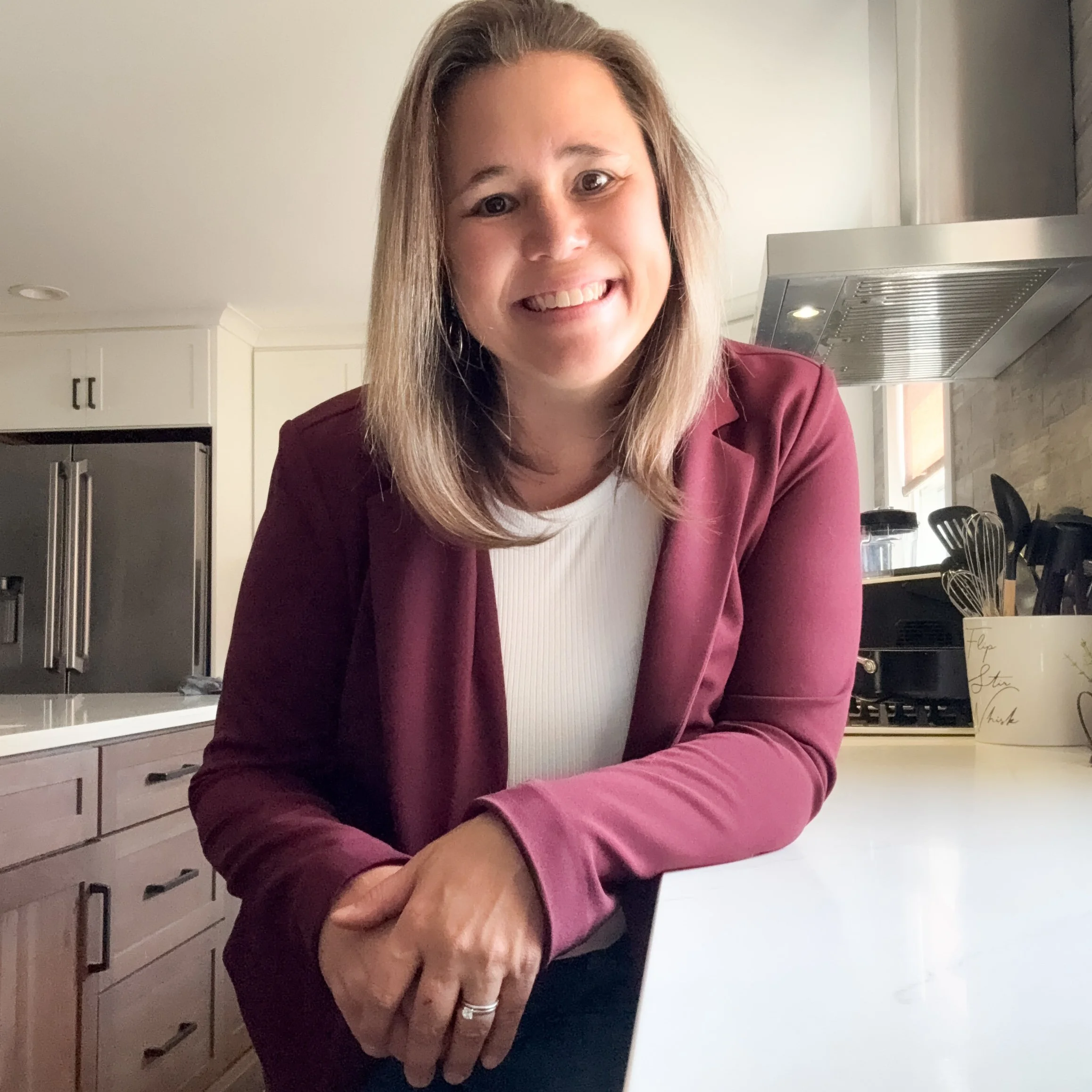 Marcie Baranich, owner of Mattison Digital, smiling in a modern kitchen, wearing a white top and burgundy blazer.
