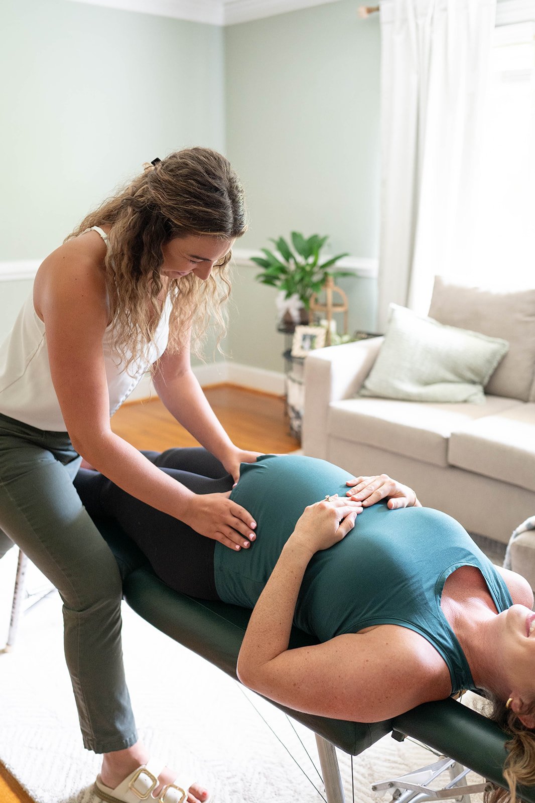 A woman receiving a chiropractic adjustment or massage from a female therapist in a cozy living room.