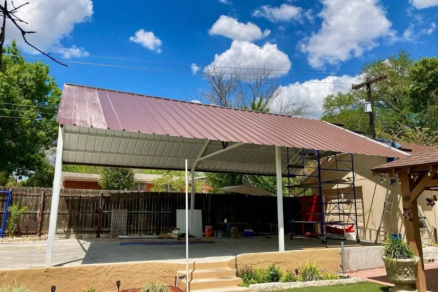 Modern metal carport attached to a brick home, featuring a sloped steel roof supported by gray posts over a concrete driveway.