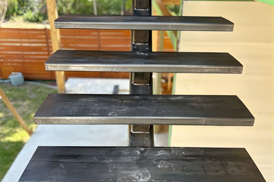 Industrial iron outdoor staircase frame with raw metal treads welded to a central support.