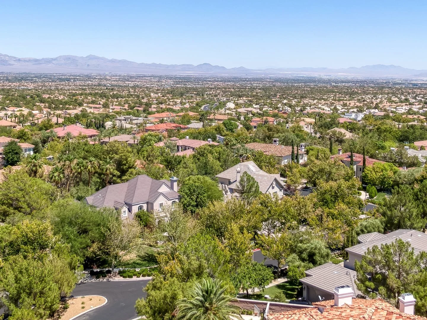 Aerial view of Mountain Trails, Summerlin, with houses, trees, and a distant mountain range under clear blue sky.