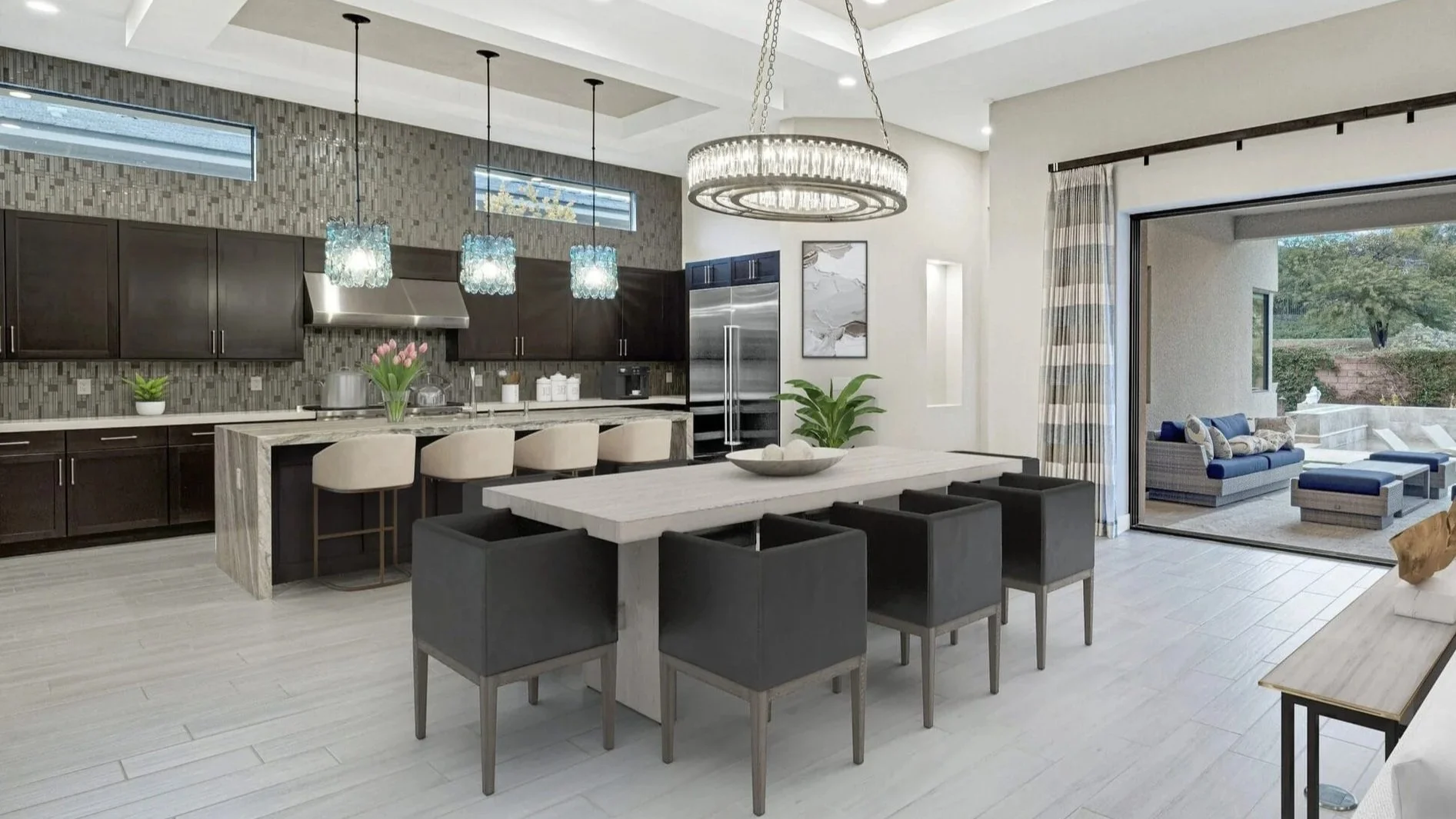 Modern open-plan kitchen and dining area with a large rectangular white dining table surrounded by black chairs, a kitchen with dark cabinets, a marble island with beige barstools, and a patio with outdoor seating visible through sliding glass doors.