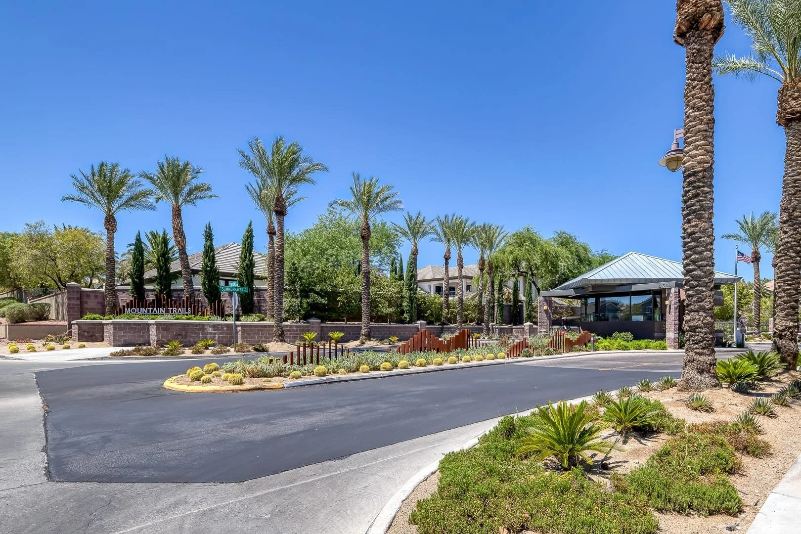 Mountain Trails, Summerlin, Gated community entrance with palm trees, bushes, and a guardhouse under a clear blue sky.