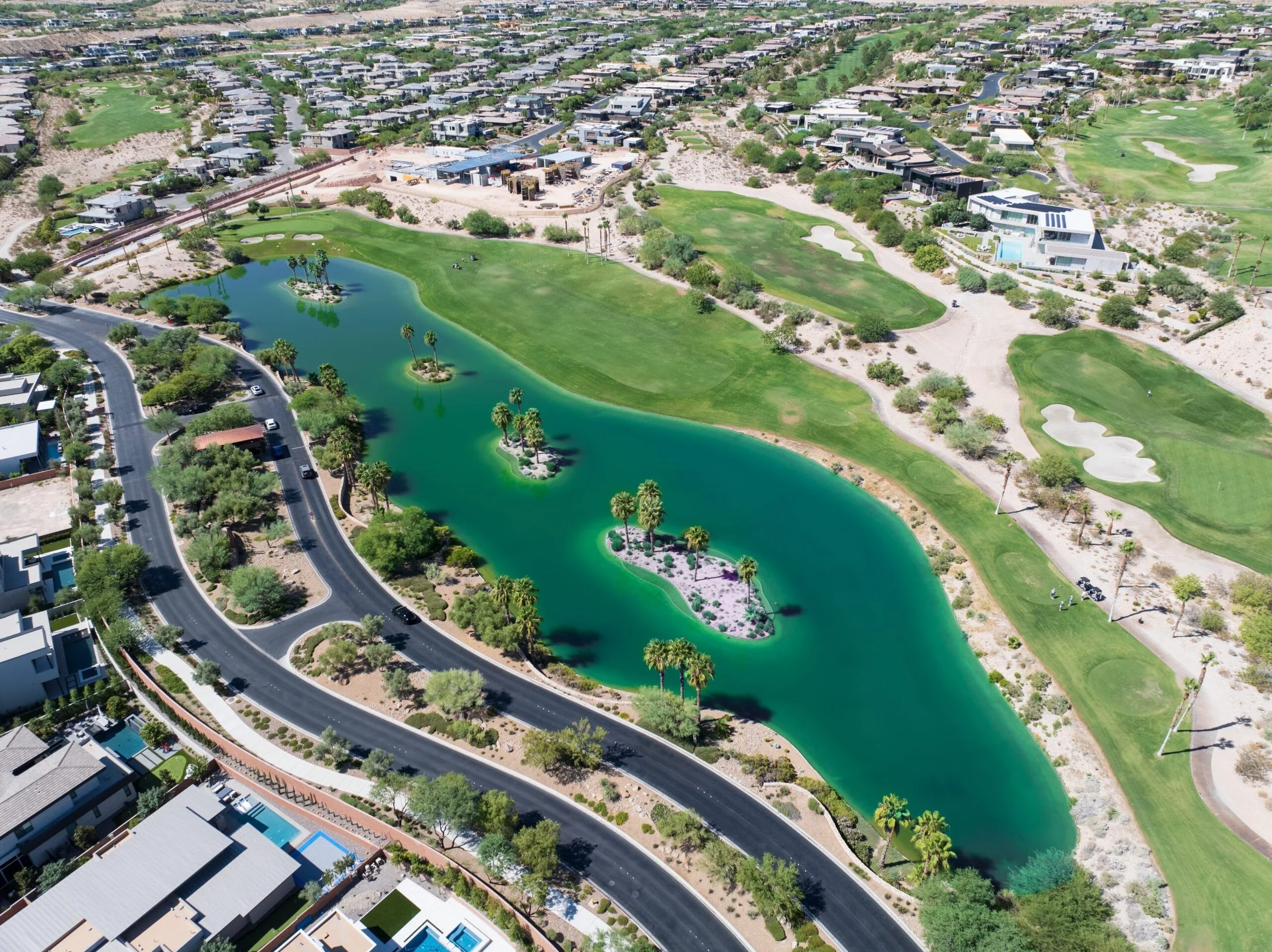 Aerial view of The Ridges with a large green golf course, a winding water feature with islands, residential homes, and a road running alongside the water.