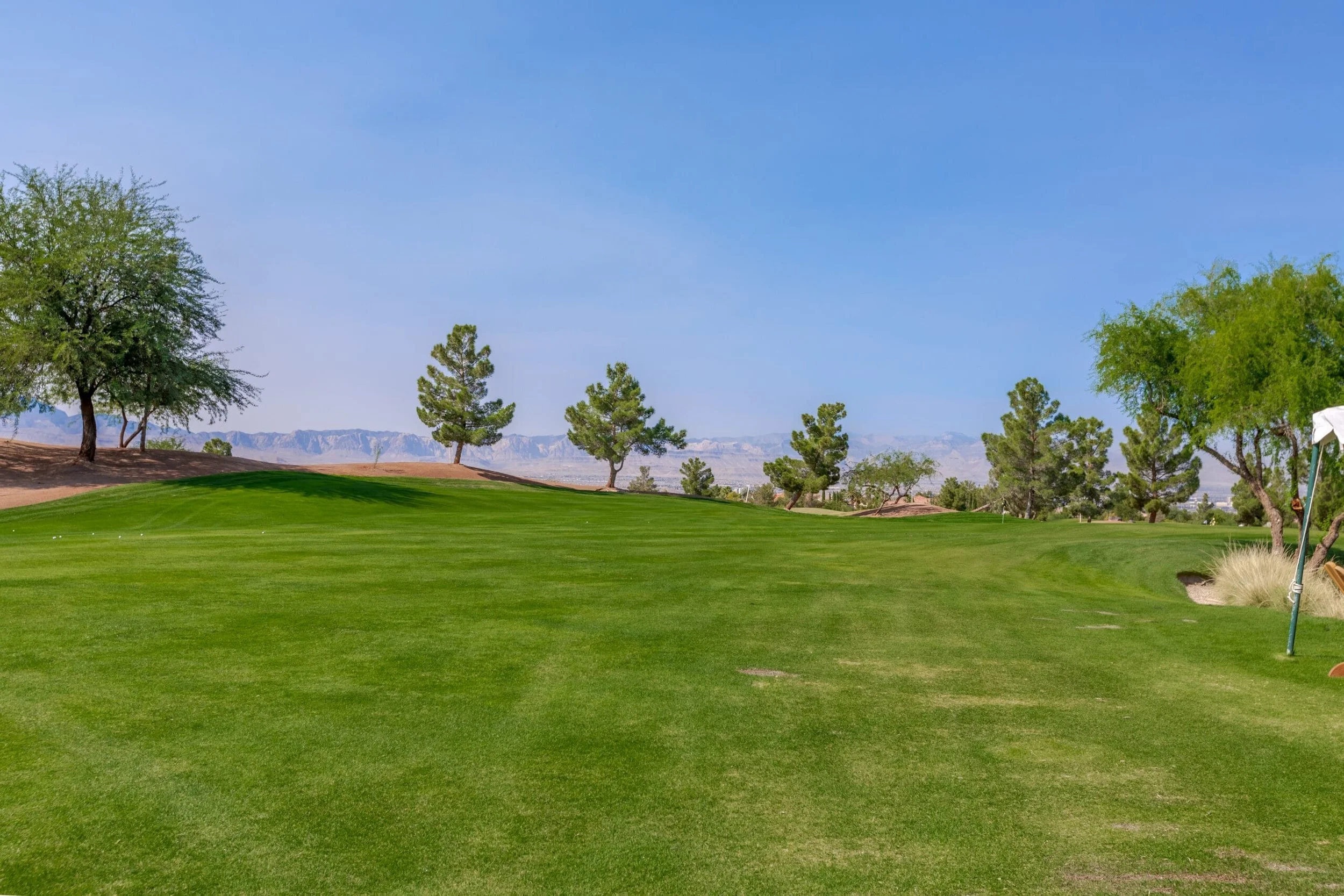 Rio Secco Golf course, Seven Hills, Henderson, with well-maintained green grass, several trees, and a distant mountain range under a clear blue sky.