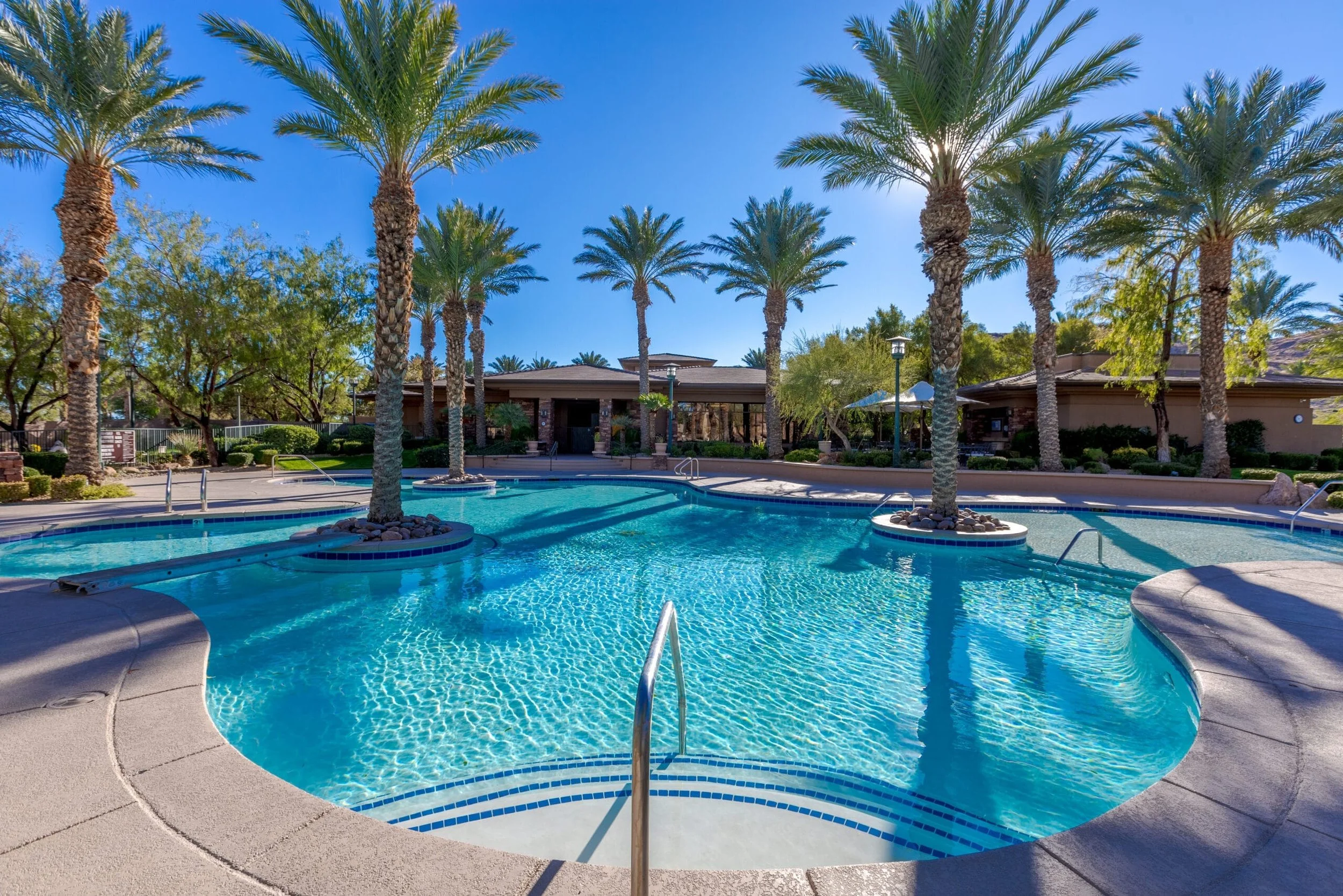 Red Rock Country Club Pool area with palm trees, lounge chairs, and a clear blue sky.