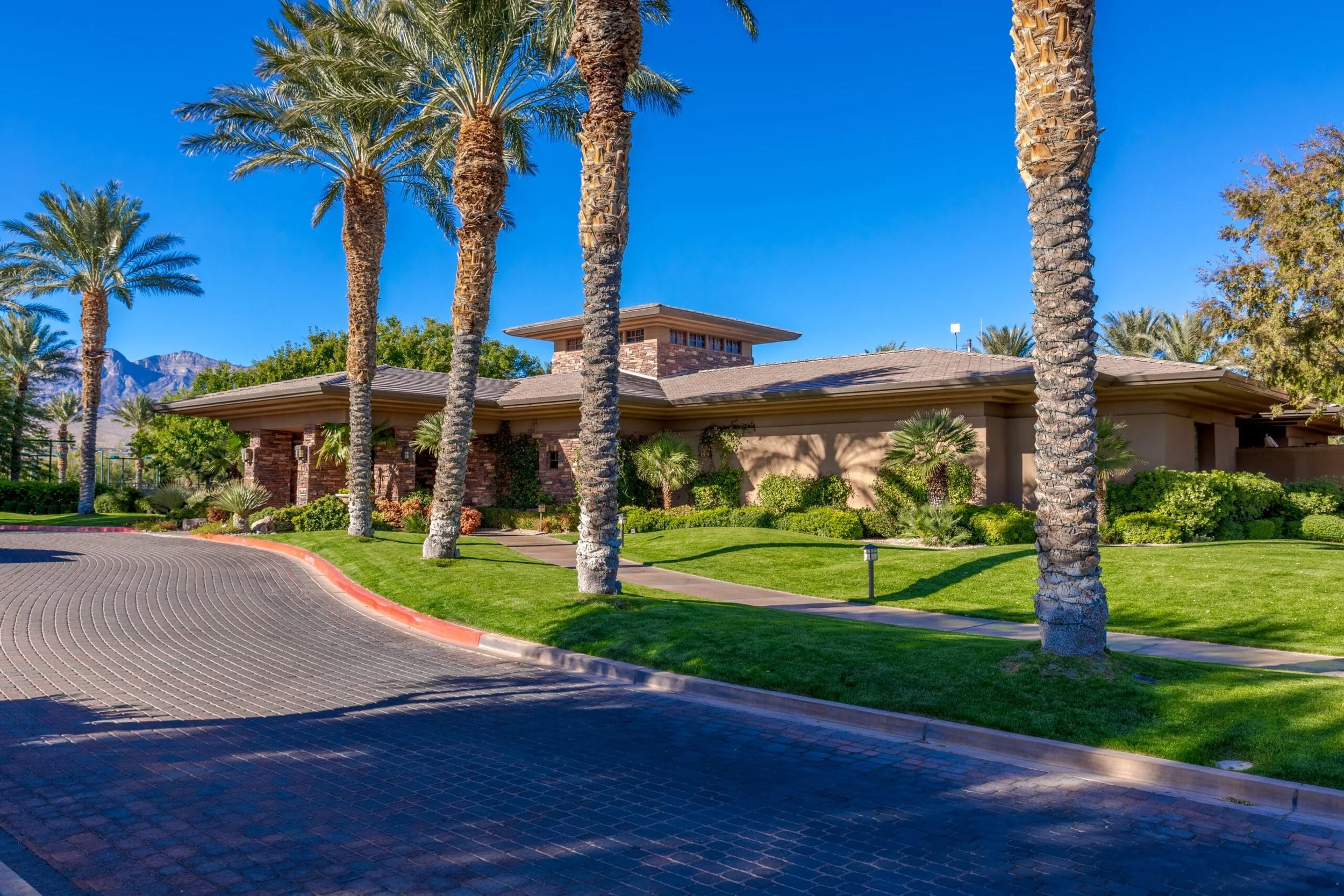 A single-story building with a flat roof surrounded by palm trees and well-maintained green lawns under a clear blue sky.