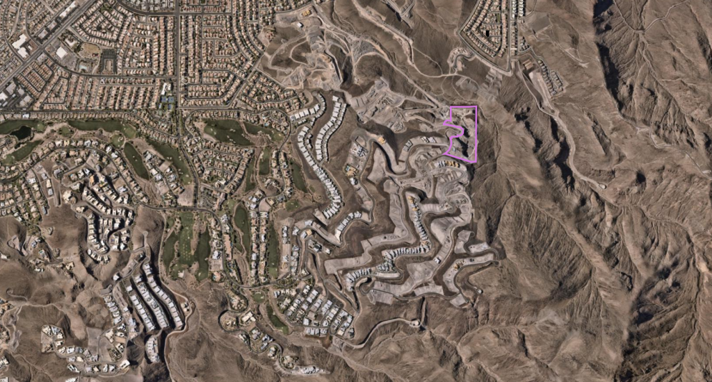 Aerial view of a residential area with winding streets and houses surrounded by arid terrain and hills.