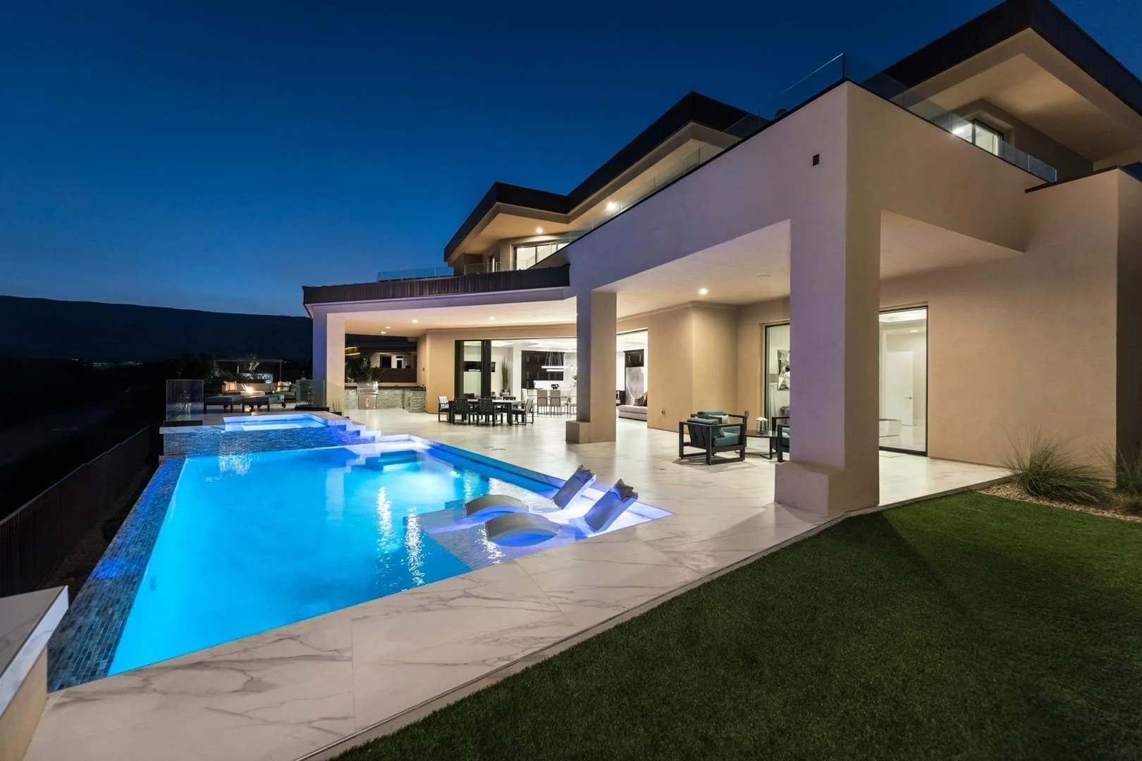 Modern The Ridges house with illuminated swimming pool and outdoor seating area at night.