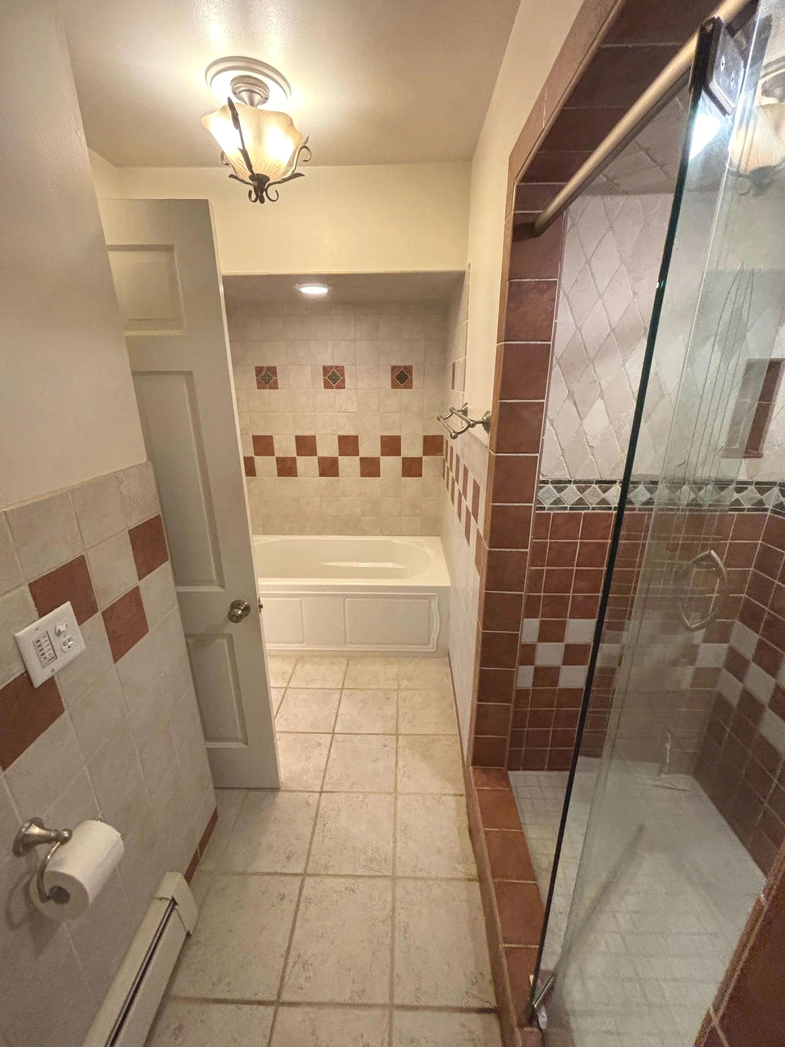 Bathroom with tiled floor, partial bathtub, glass shower enclosure, and a ceiling light fixture.