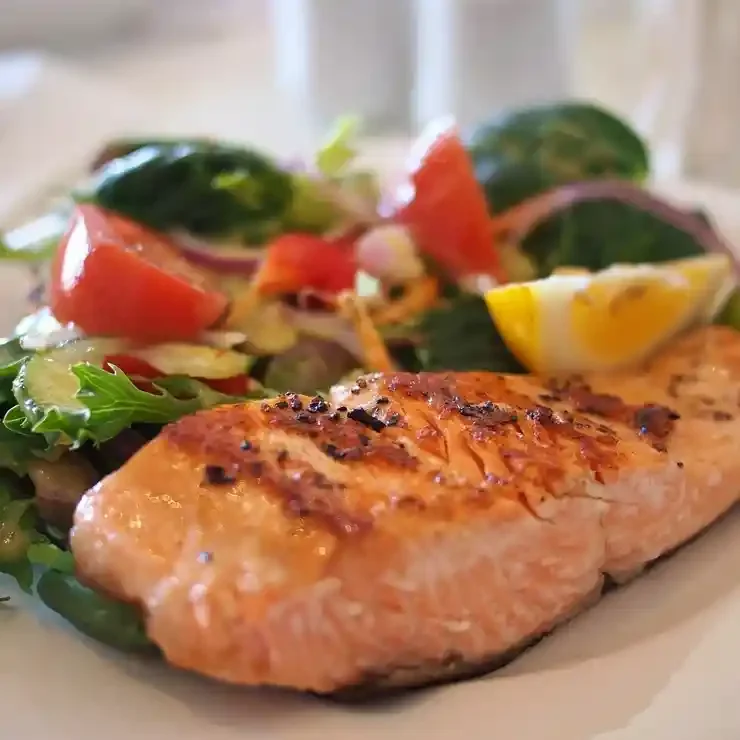 Grilled salmon fillet with a side salad of tomatoes, lettuce, onions, and lemon wedge