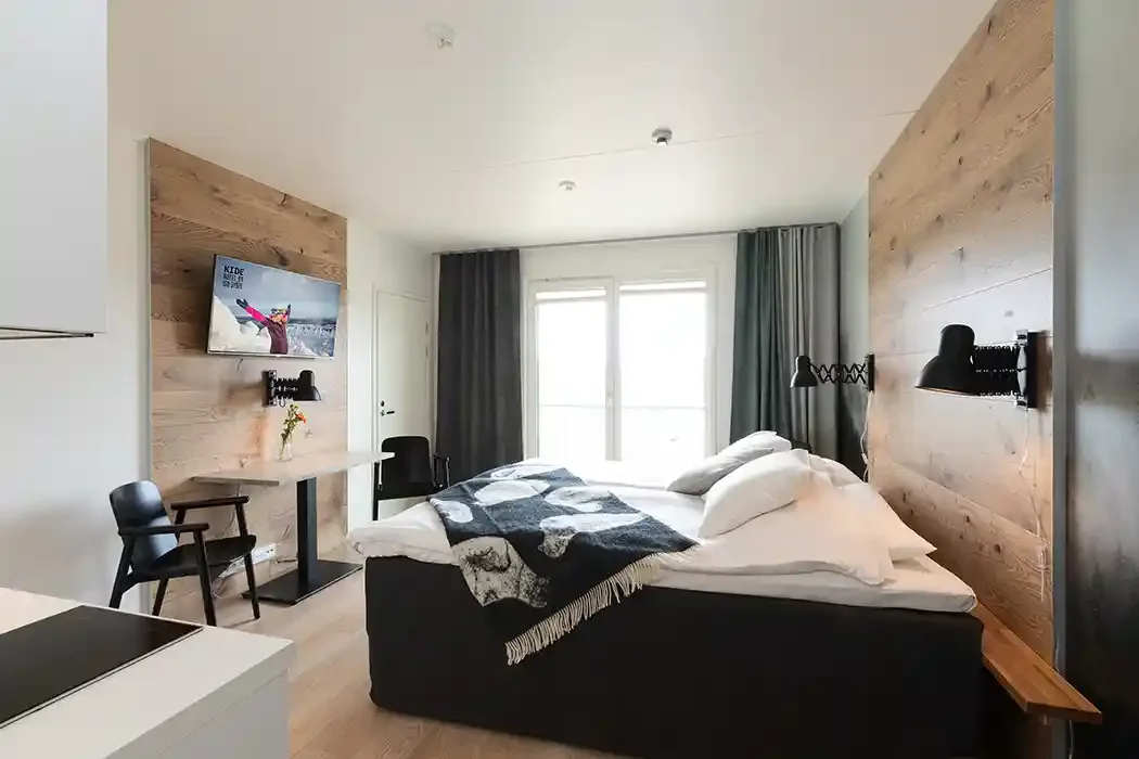 Modern bedroom with a bed, a window with curtains, a wall-mounted TV, a small desk, and chairs