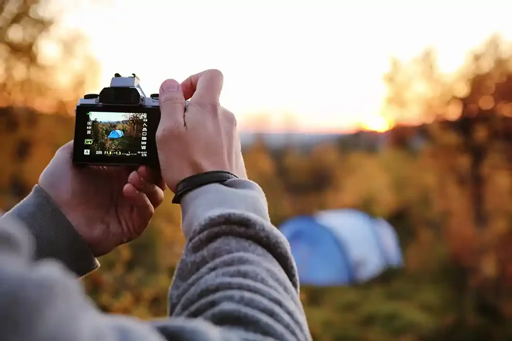 Person taking a photograph of a campsite with a tent at sunset