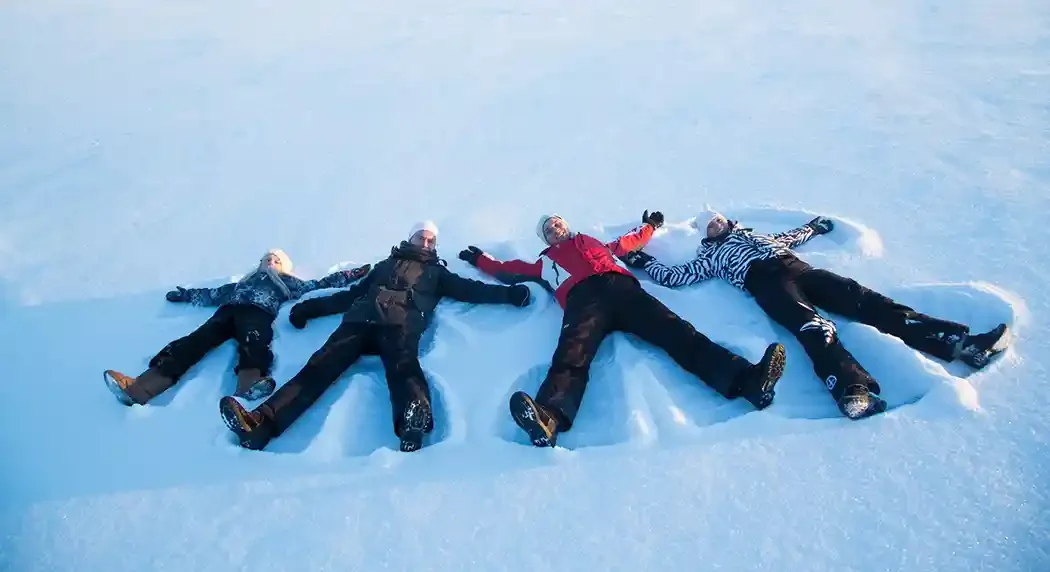 Four people lying on their backs in the snow, making snow angels and smiling.