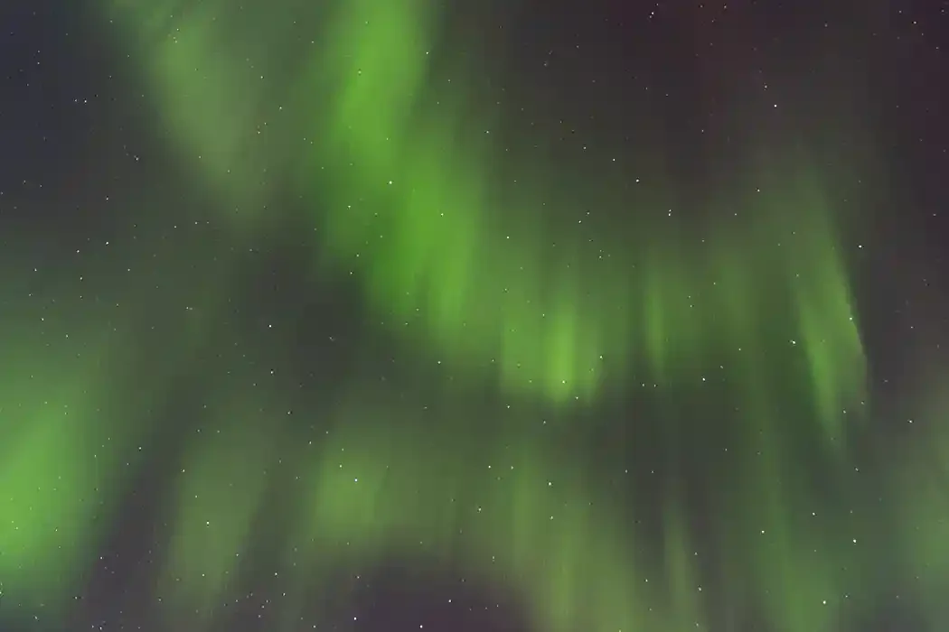 Northern lights or aurora borealis in the night sky with green and faint red hues and numerous stars.