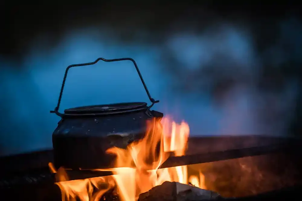 A black kettle on an open fire with flames.