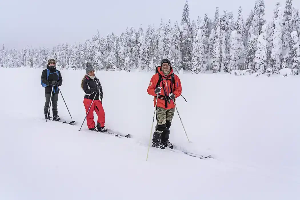 Three people snowshoeing in a snowy landscape with snow-covered trees in the background.