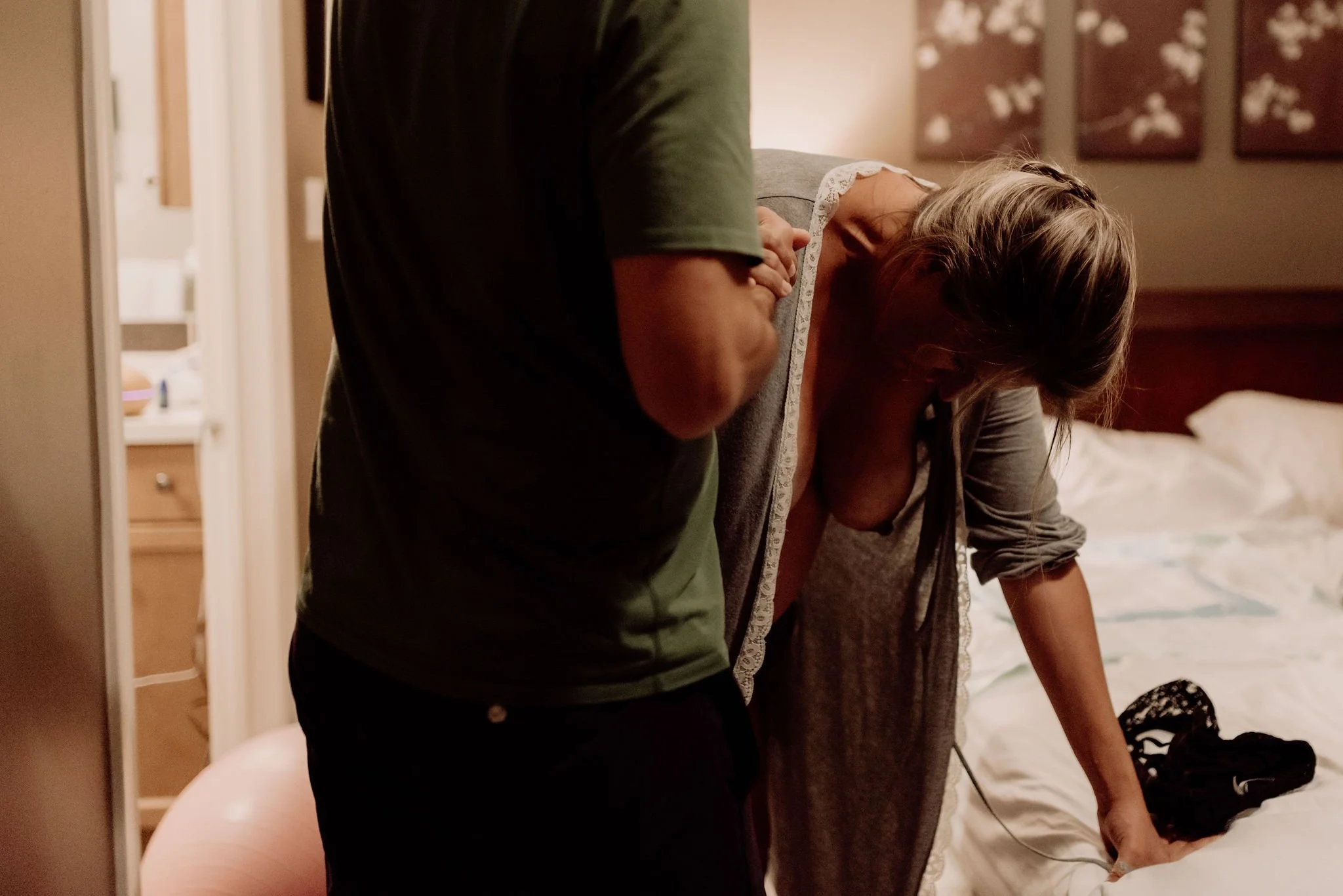 Pregnant woman leaning over a bed while a partner supports her while she is in labor.