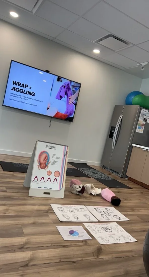 Childbirth education classroom with a presentation about labor positions, fetal development display, birthing models, and instructional handouts.