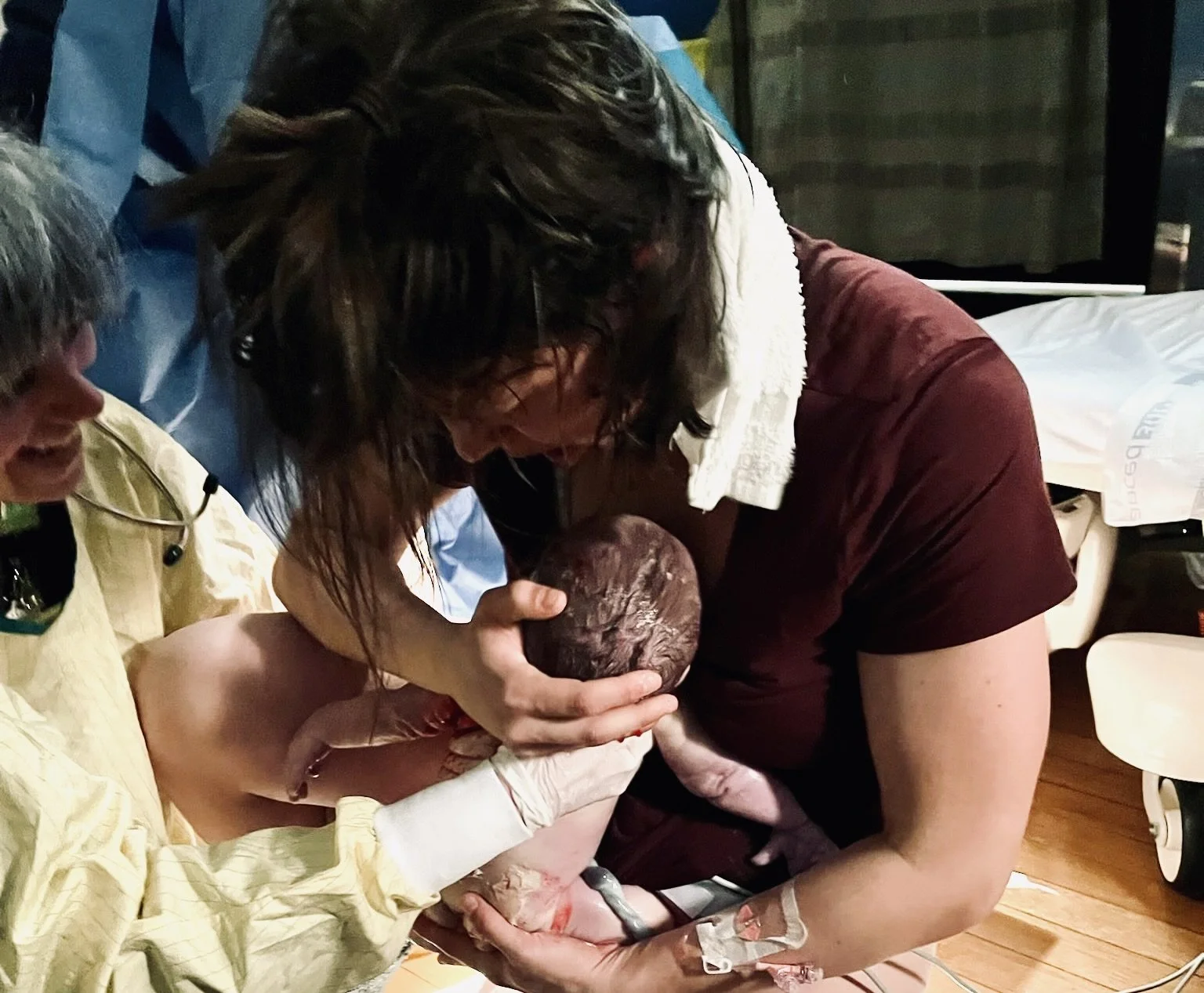 Midwife assisting a mother during a home birth as she holds her newborn baby.