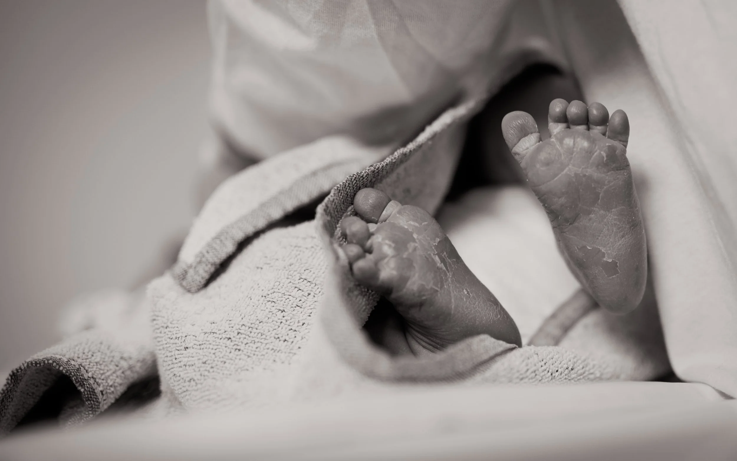 Black-and-white close-up of a newborn baby's feet resting on a soft towel.
