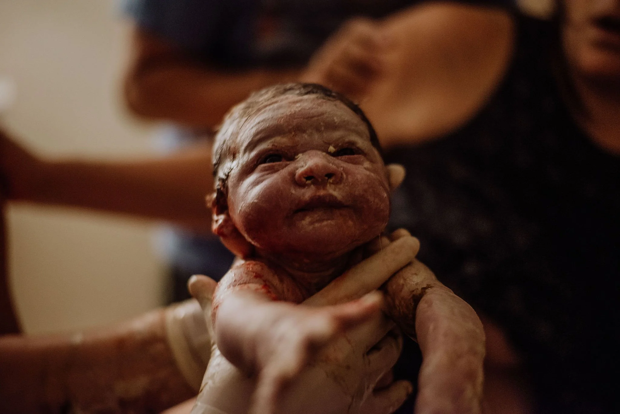 Newborn baby being gently held by an adult in a dimly lit room