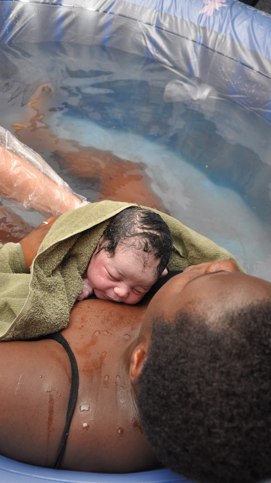 Newborn baby resting on a parent’s chest in a birthing pool, wrapped in a towel