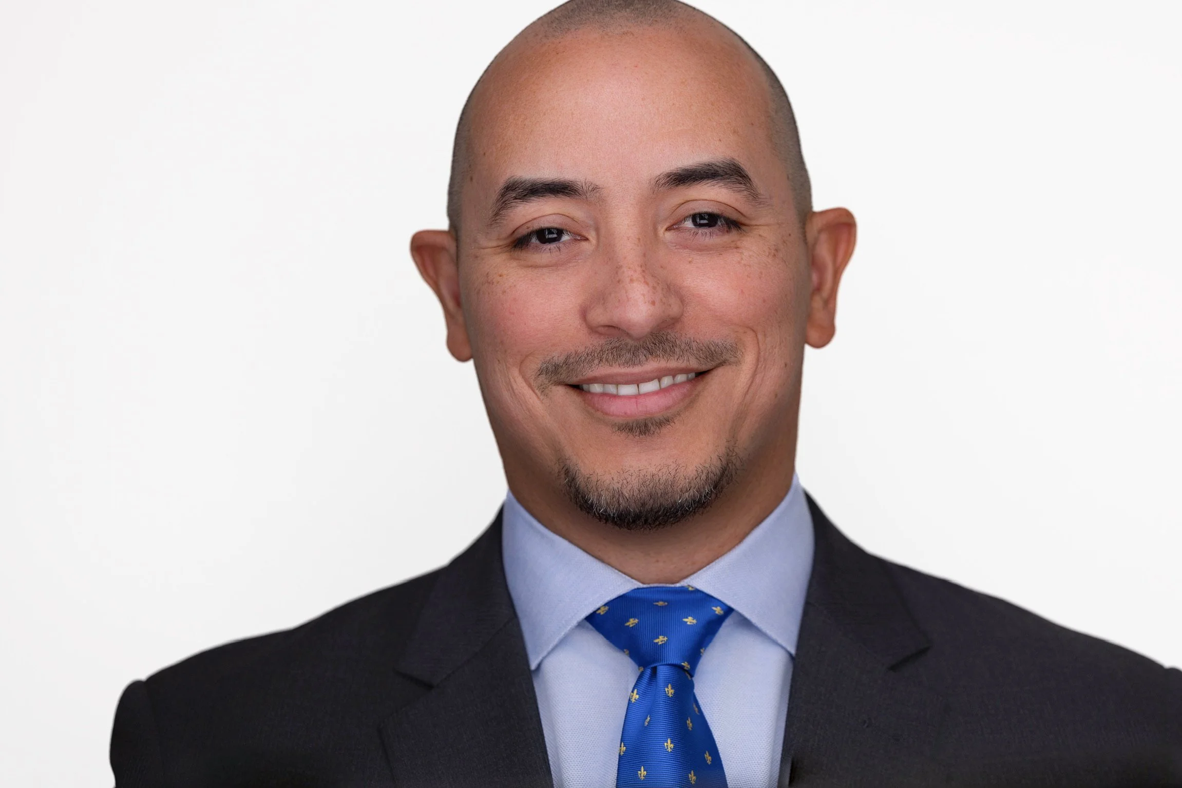 Headshot of a Victor Velez, wearing a suit and tie, smiling, with a bald head and light skin, against a white background.