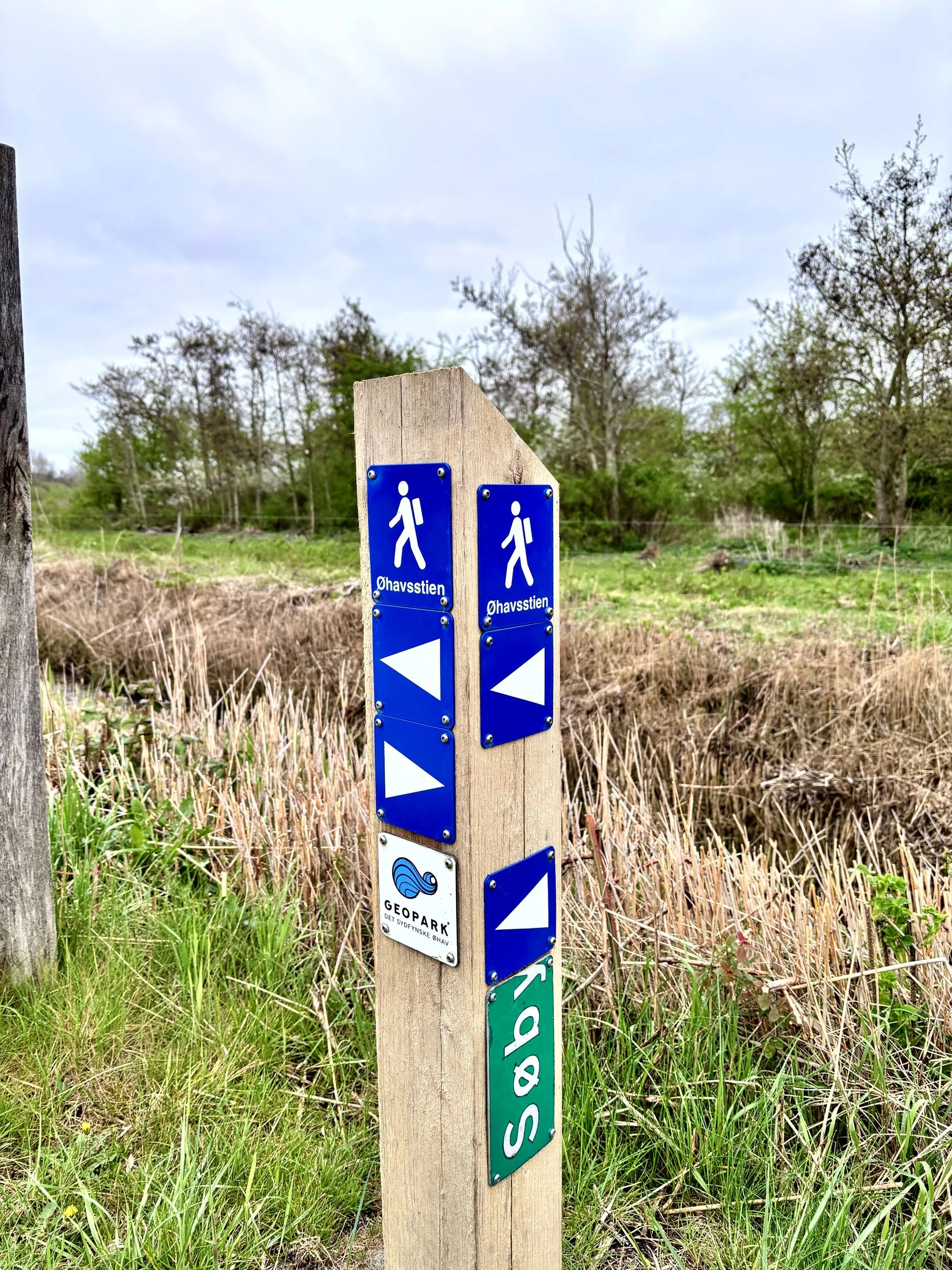 Ein schlichter Holzpfosten weist den  wanderbaren weg über die Insel Ærø. Unweit des ALTEN PFRRHAUS findet man bereits ruhige Wege durch die Natur, bestens geeignet für CEOs und Top-Performer um einmal die Gedanken baumeln zu lassen