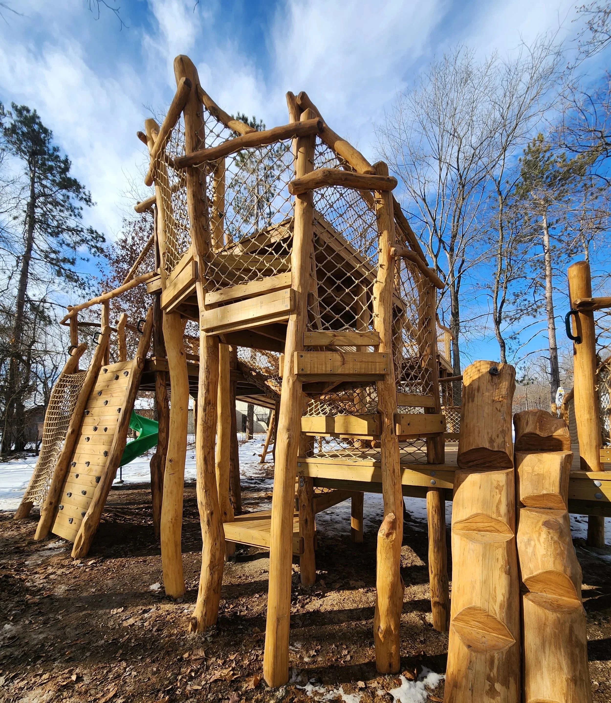 Inclusive playground at the Lafayette YMCA recreation area with connected decks, bridges, slides, a cargo climber, climbing wall, and log jam play features in Lafayette, Indiana.