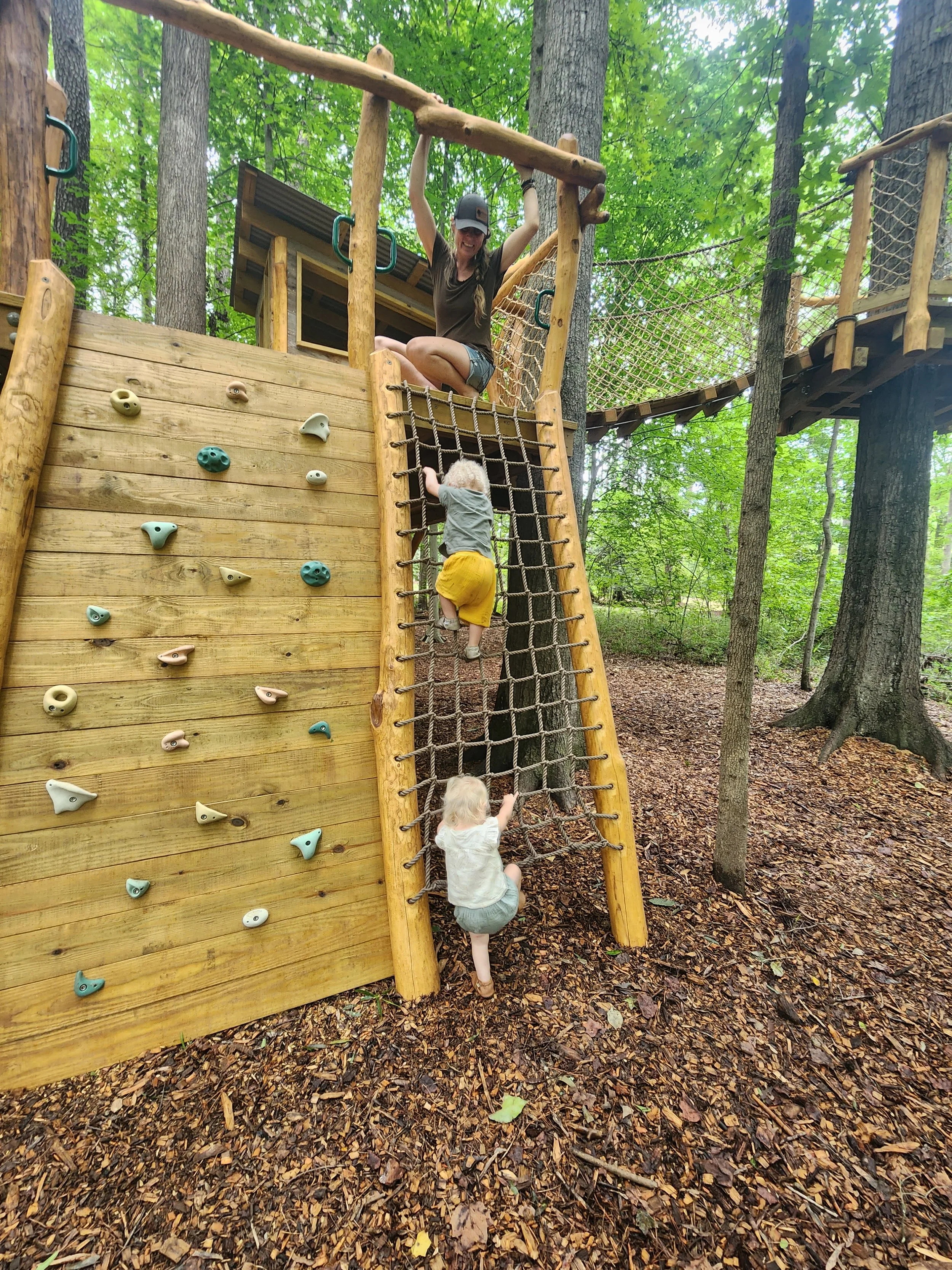 Two children climbing a custom black locust playground with a climbing wall and cargo net in Cary, North Carolina.