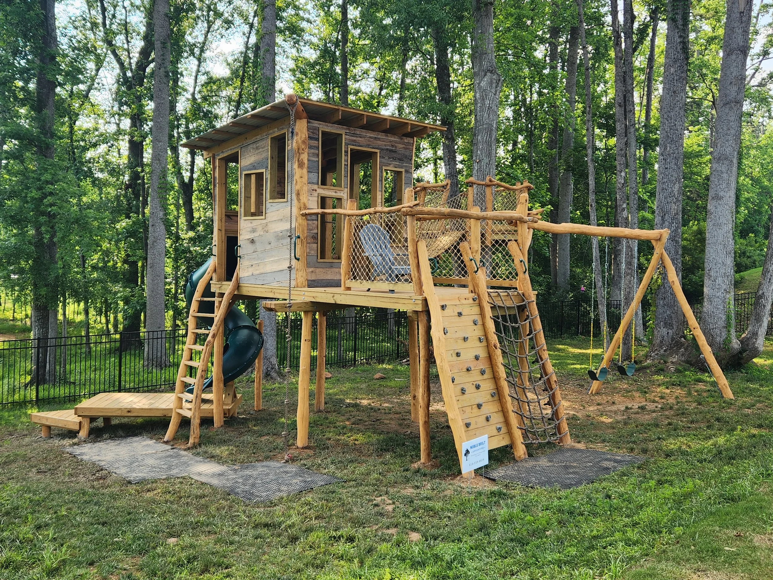 Custom treehouse with a slide, climbing wall, bird's nest, rope climb, and swing set in Indian Land, South Carolina.