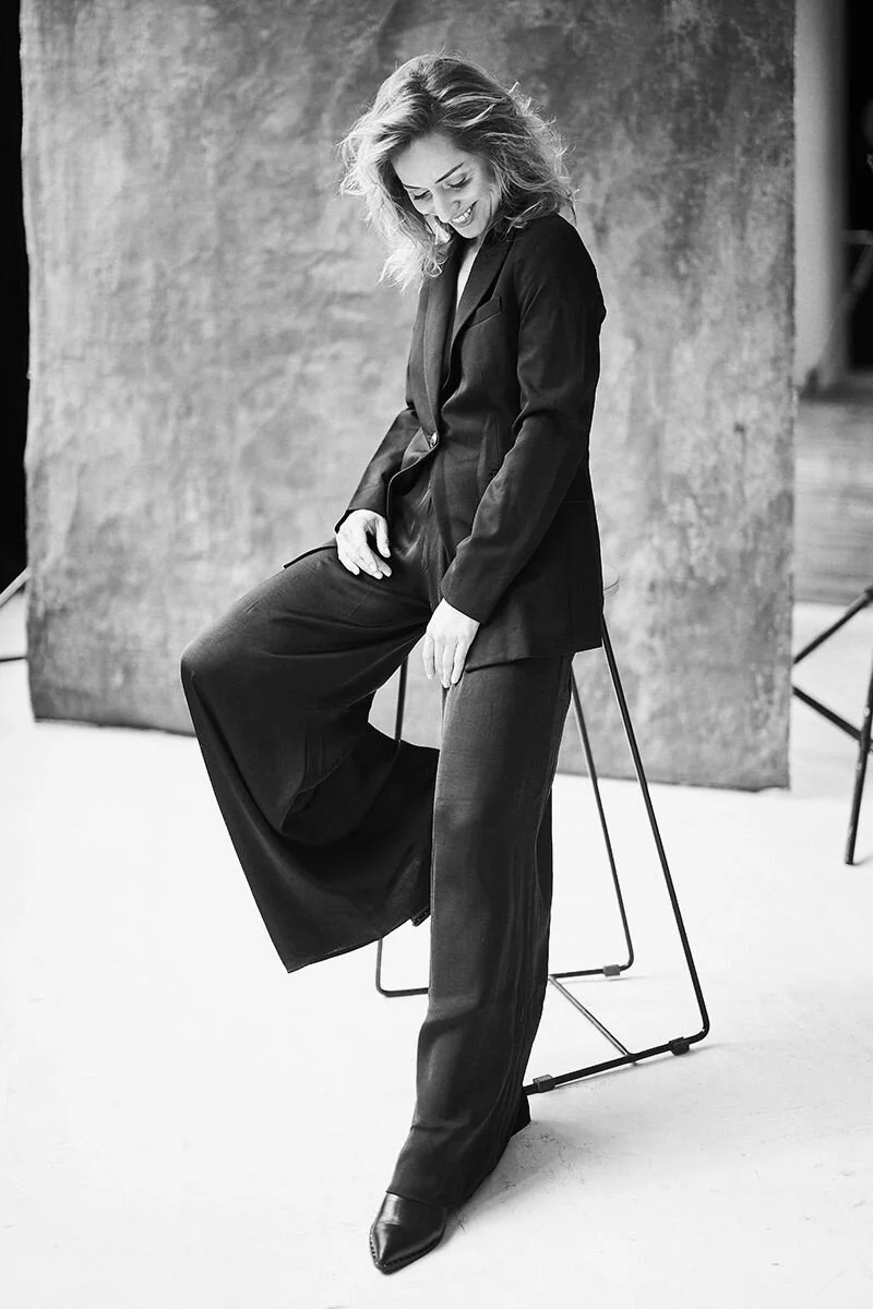 Woman_in_Black_Suit_Sitting_on_Chair_with_Smiling_Expression.jpg