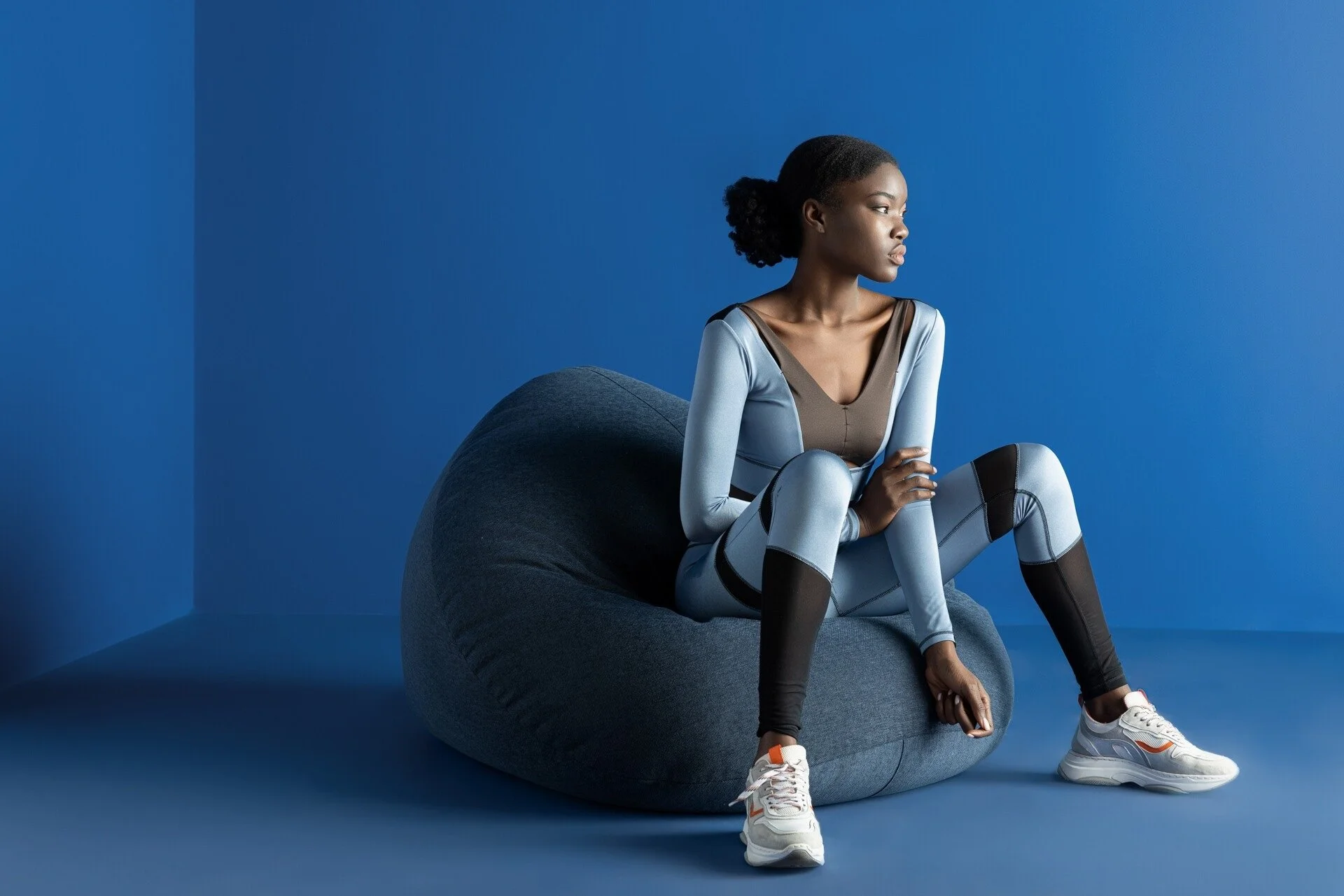 Une femme portant des vêtements de sport bleus et noirs est assise sur un pouf bleu. Cette photo a été prise à Zurich par un photographe professionnel.