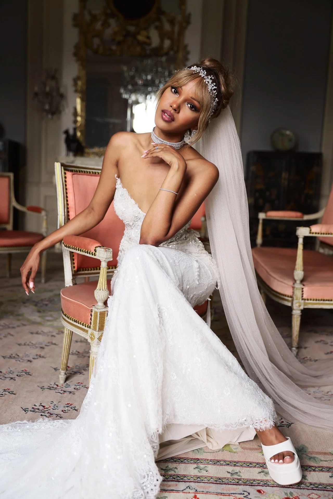 Jeune mariée en robe blanche et voile, assise dans une pièce élégante.jpeg